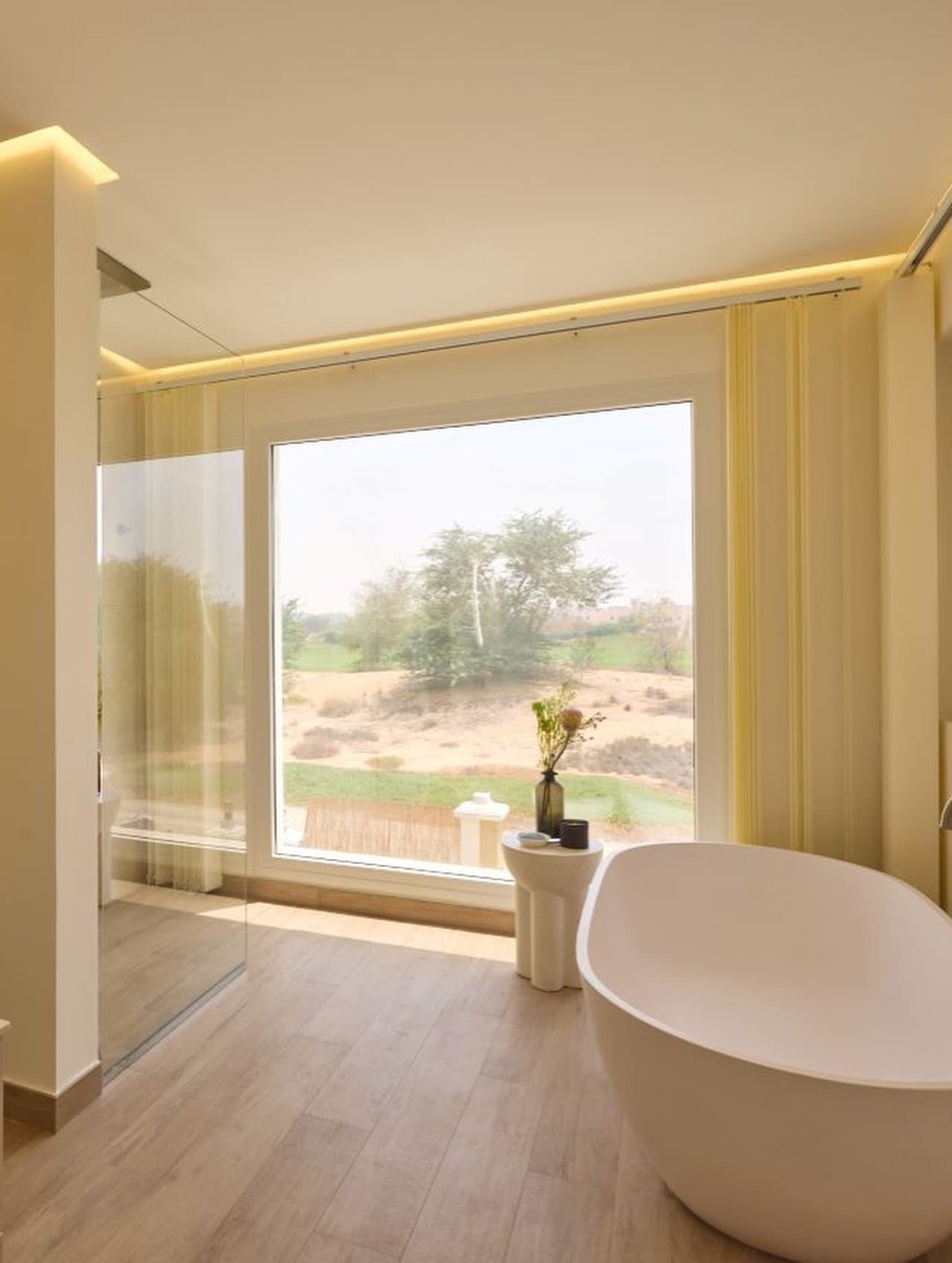 The ensuite's freestanding tub is angled toward a full-height view of desert and greenery.