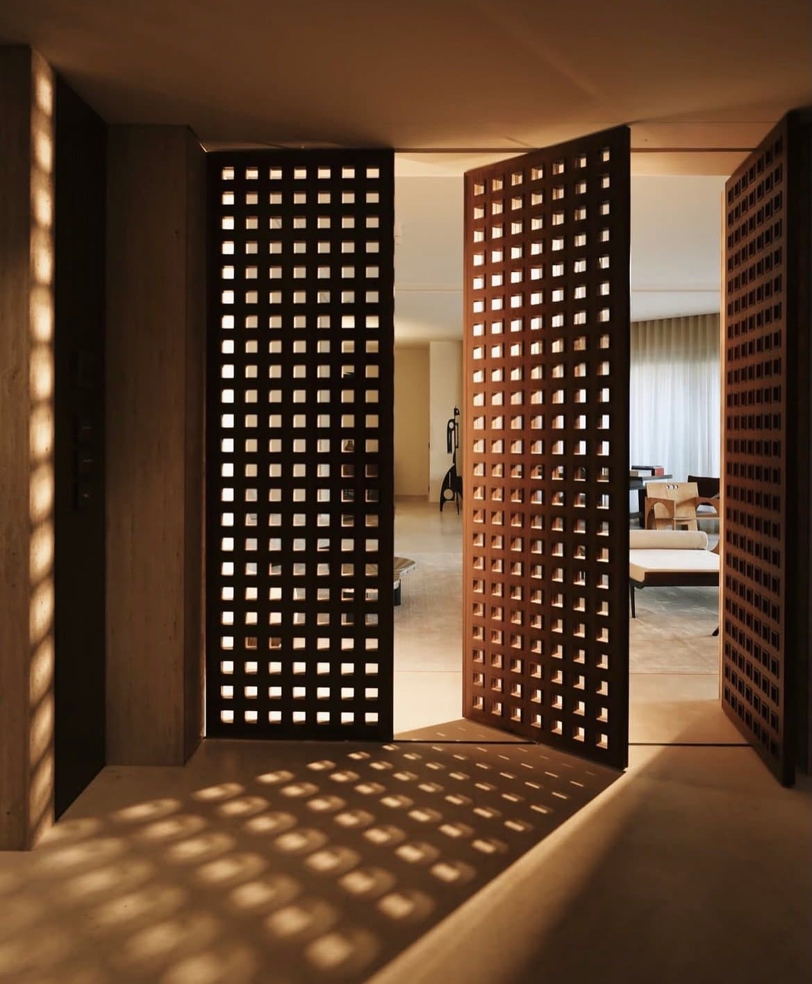 Perforated wooden doors at the entry translate light into pattern across the stone floor.