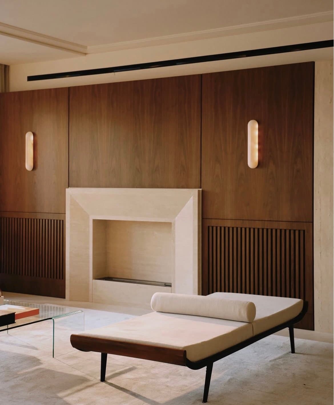 A walnut wall, travertine fireplace and fluted grille panels anchor the room in centred symmetry.