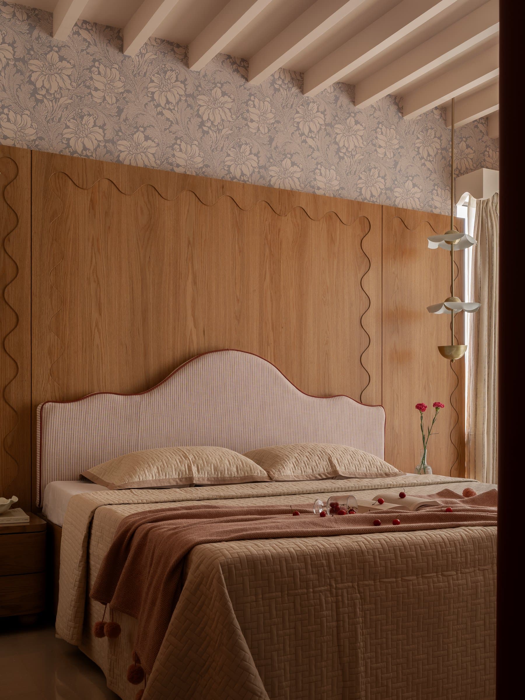 The master bedroom, where a scalloped headboard edged in oxblood piping sits against a wood-panelled wall inset with wavy grooves