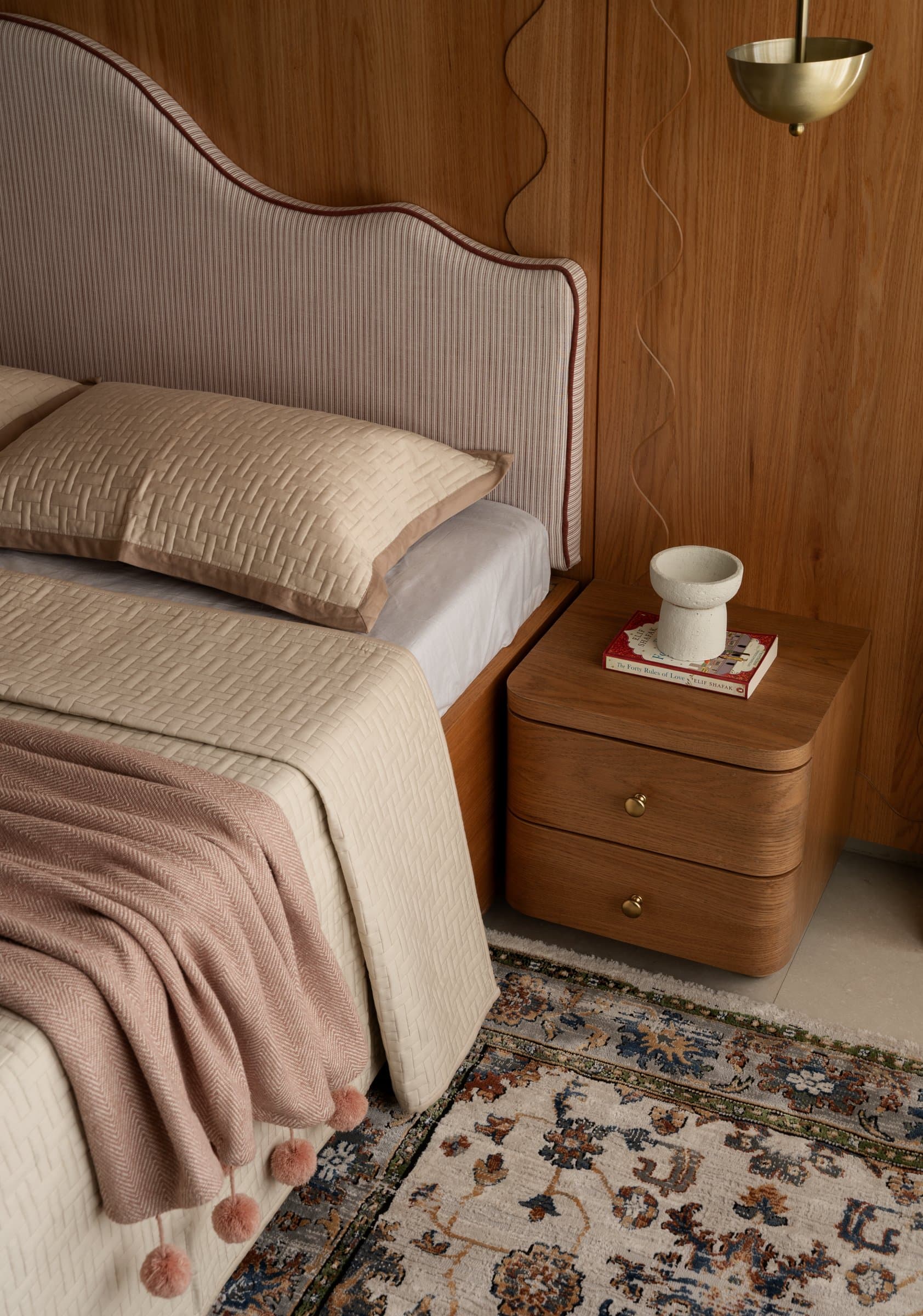 A closer view of the bed's scalloped headboard and rounded bedside cabinet, grounded by a vintage floral rug