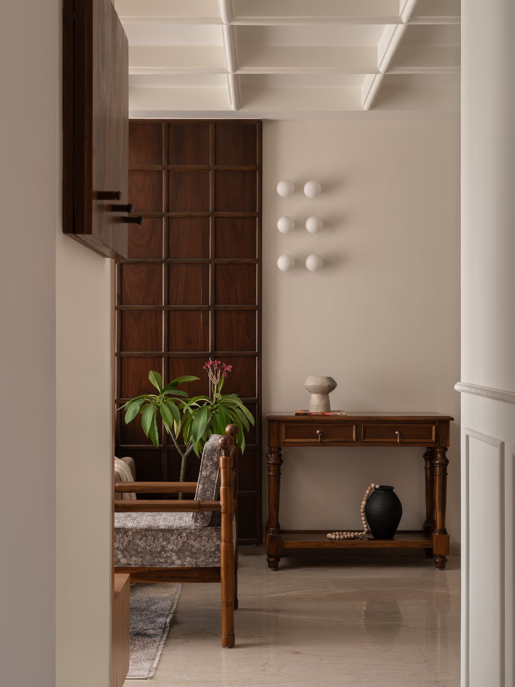 The entry, where a grid-panelled teak wall and a slim console with turned legs establish the home's material language