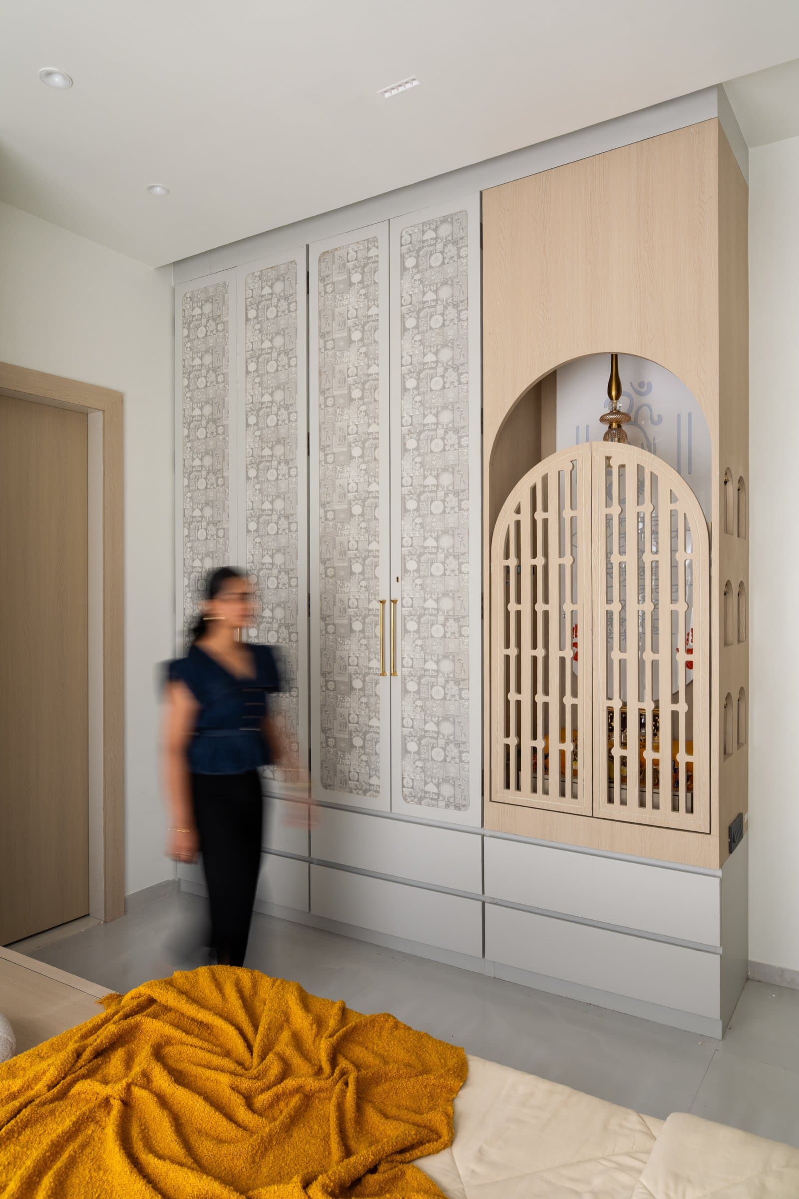 The pooja unit, its arched screen doors in blond wood flanked by cabinetry with softly patterned wallpaper insets