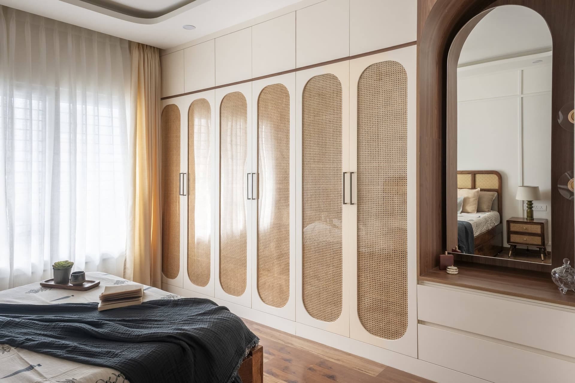 The wardrobe wall, where six rounded cane panels translate a decorative motif into daily-use joinery