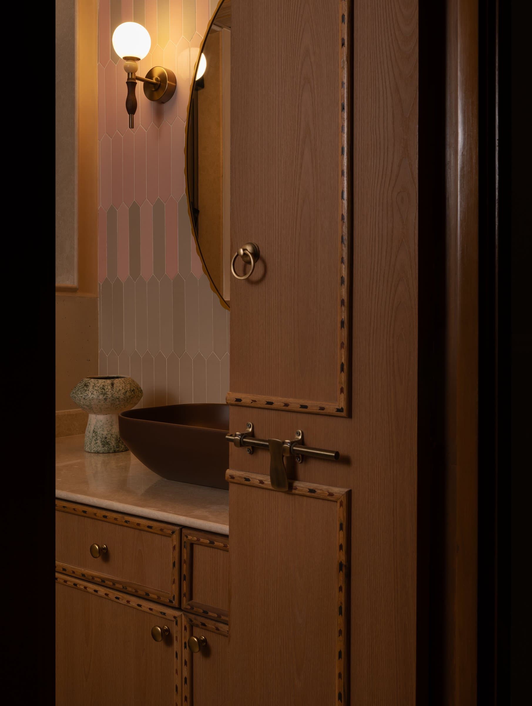 The second bathroom, where a globe sconce and matte oxblood basin sit against picket-shaped pale pink tiles