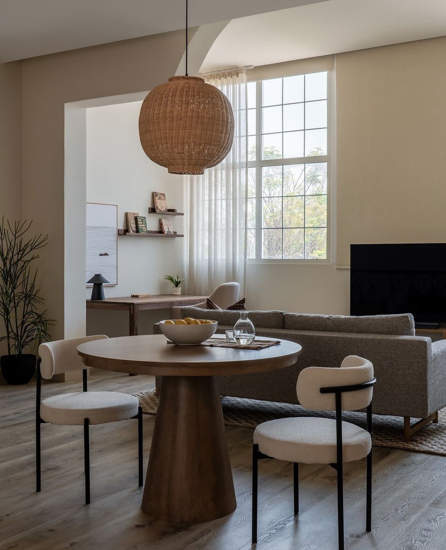 The dining table sits beneath an oversized woven rattan pendant, open to the living zone beyond.