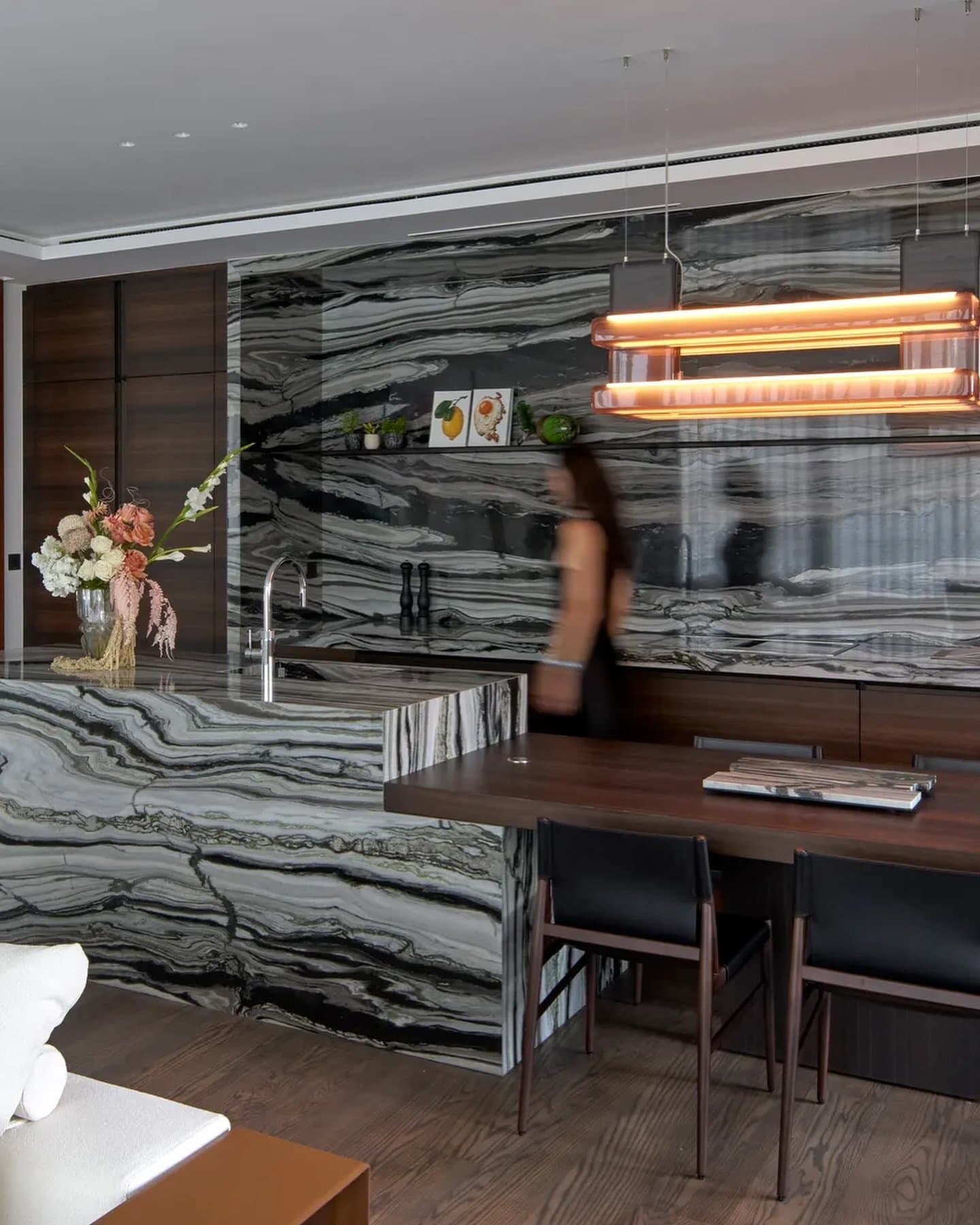 In the kitchen, bookmatched dark stone wraps island and backsplash, met by walnut cabinetry and a single amber pendant.