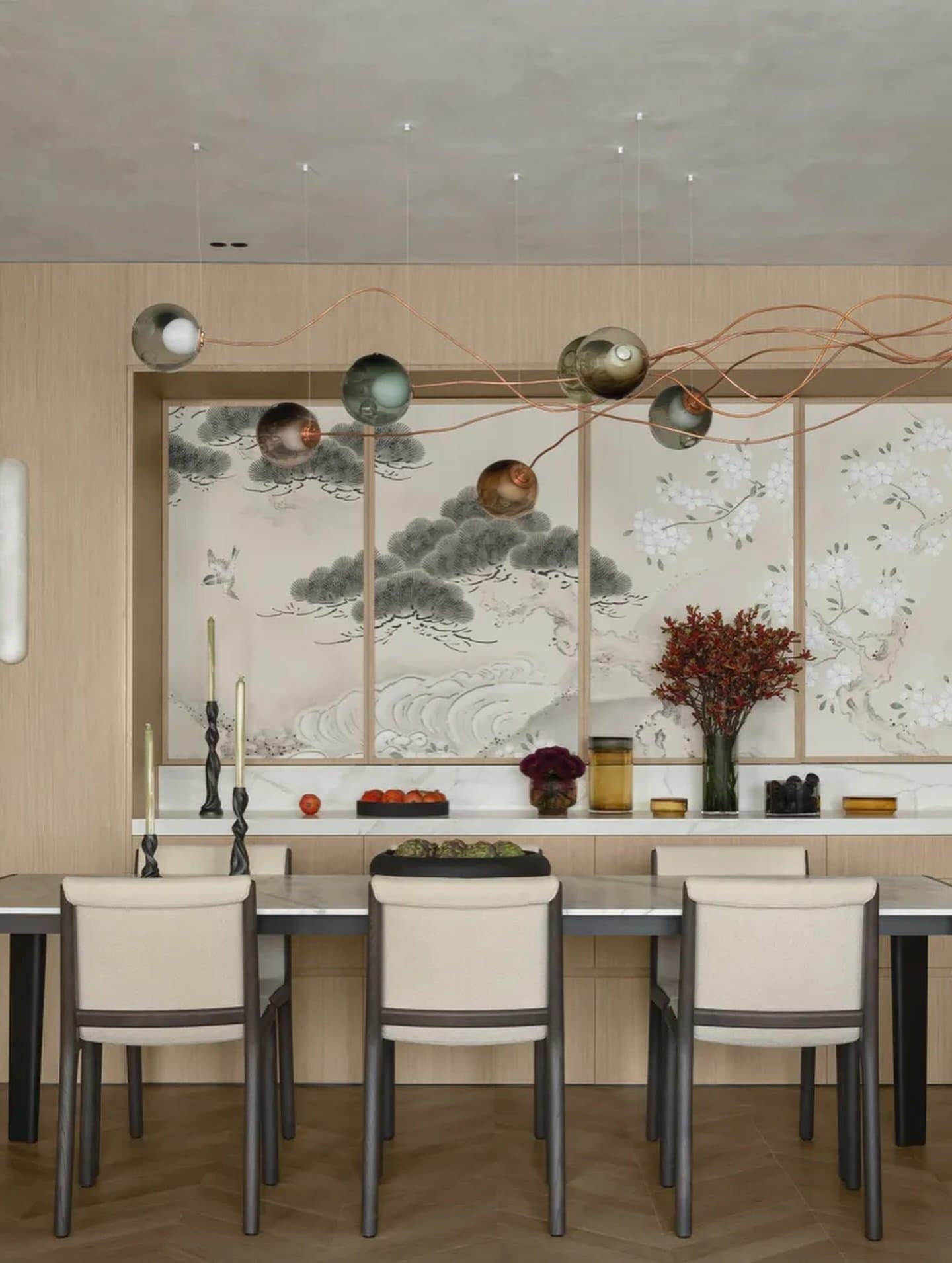The dining wall's pine and blossom mural sets a soft, ink-wash counterpoint to the room's tonal restraint.