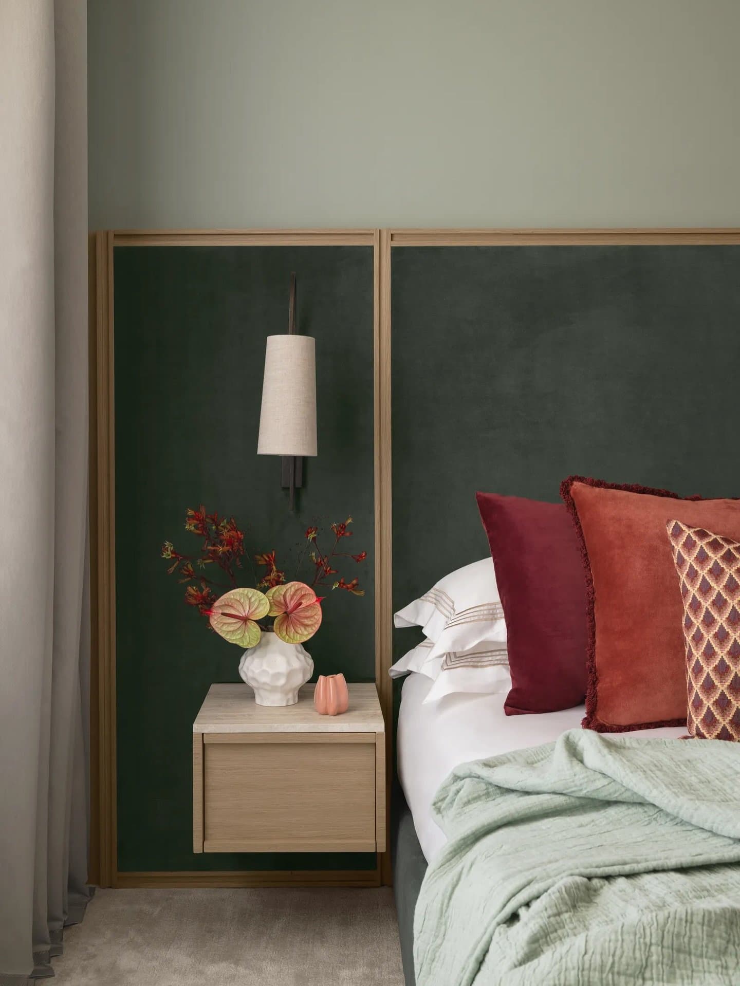 A dark green velvet headboard extends into a floating wood-and-stone nightstand, framing the bedroom's most tactile vignette.
