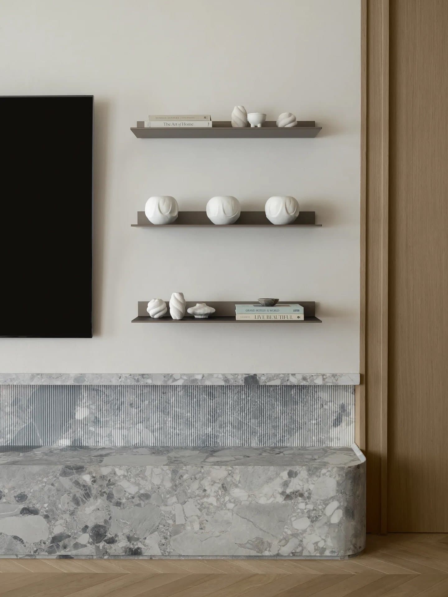 A media wall in fluted marble, limewashed plaster, and honed stone absorbs function into architectural continuity.