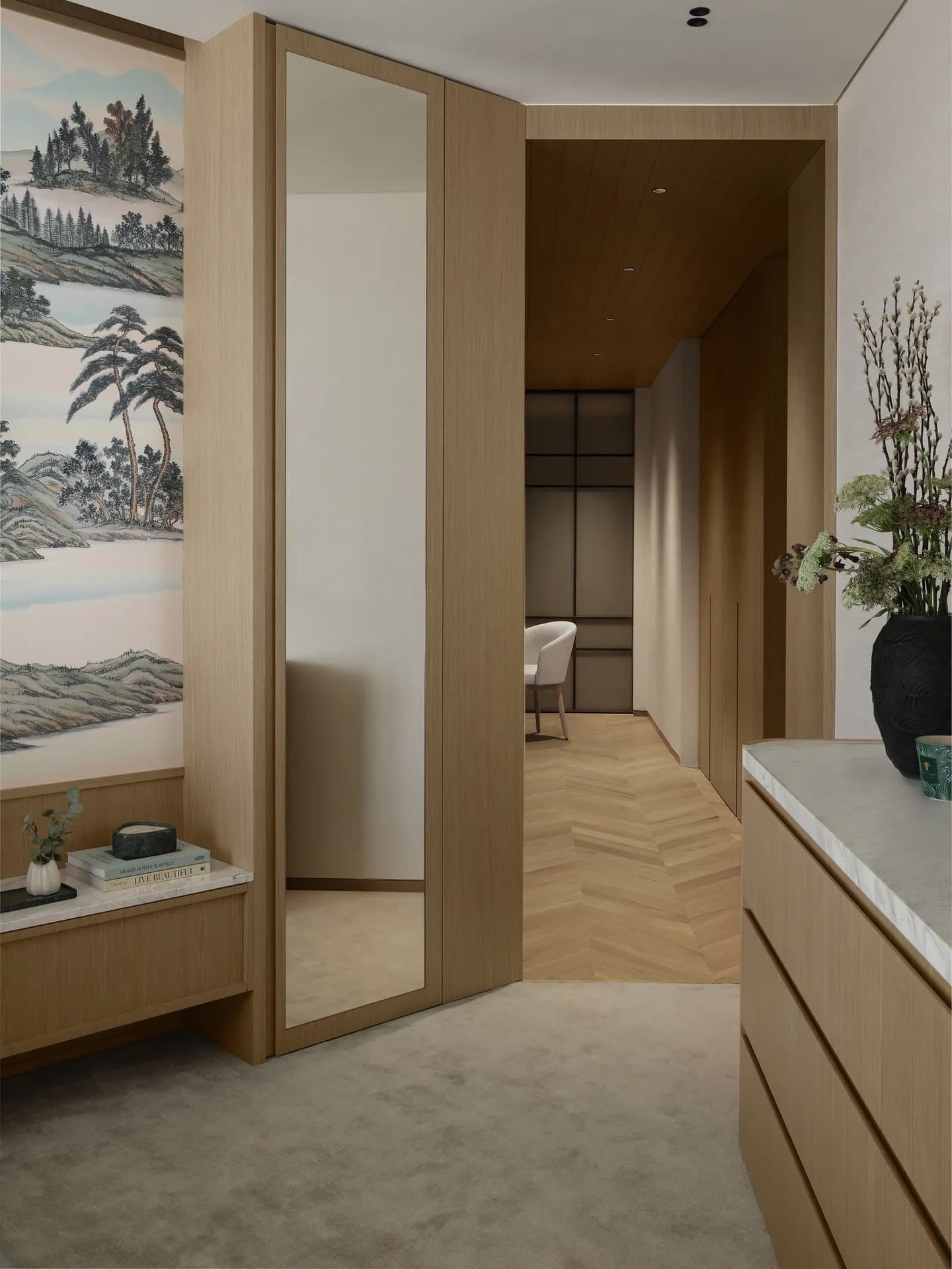 A dressing passage in warm wood veneer leads through mirrored doors and a hand-painted mural to a distant seating nook.