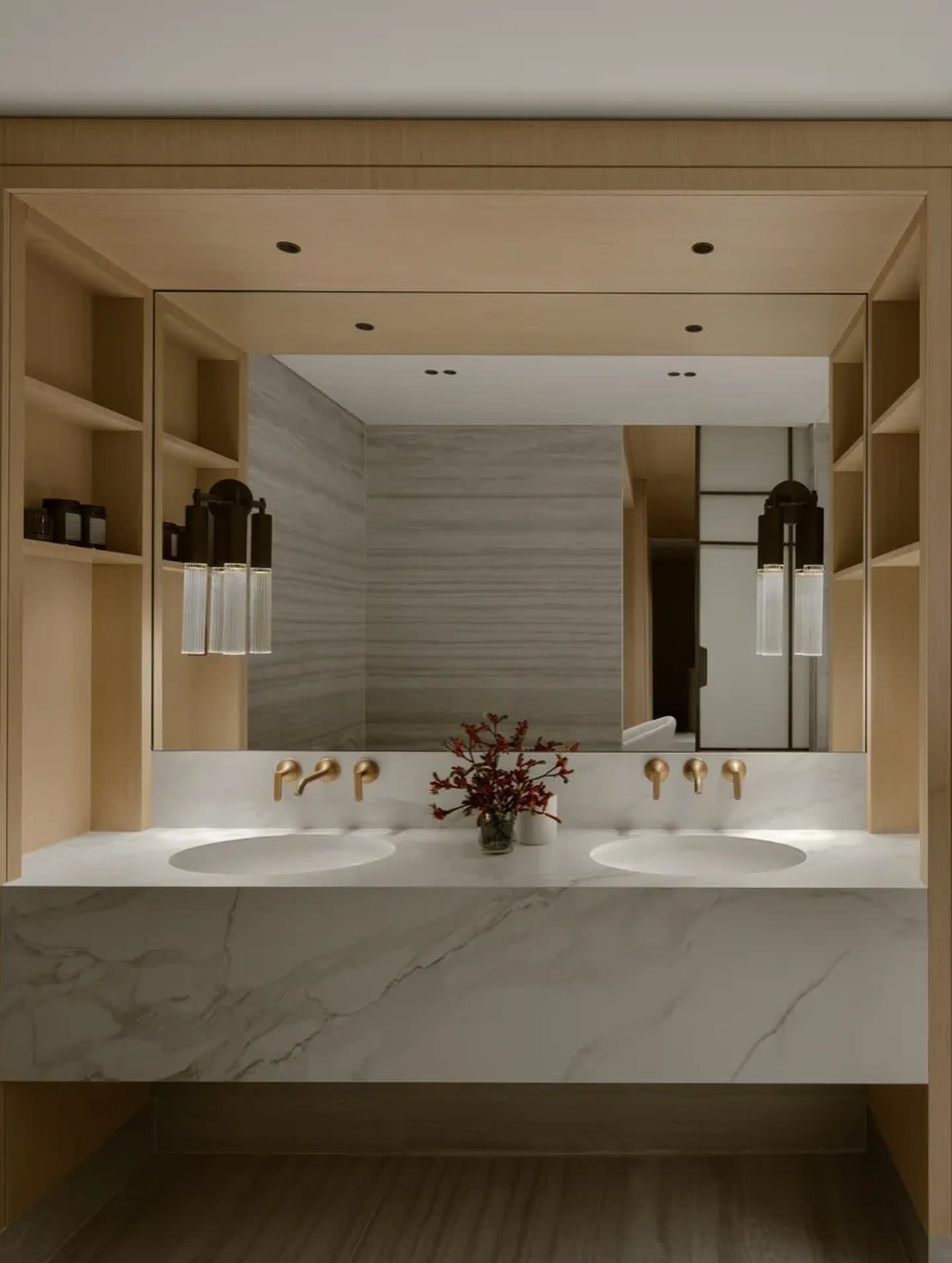 The bathroom's waterfall-edge marble vanity is warmed by a deep wood surround and slim brass sconces.