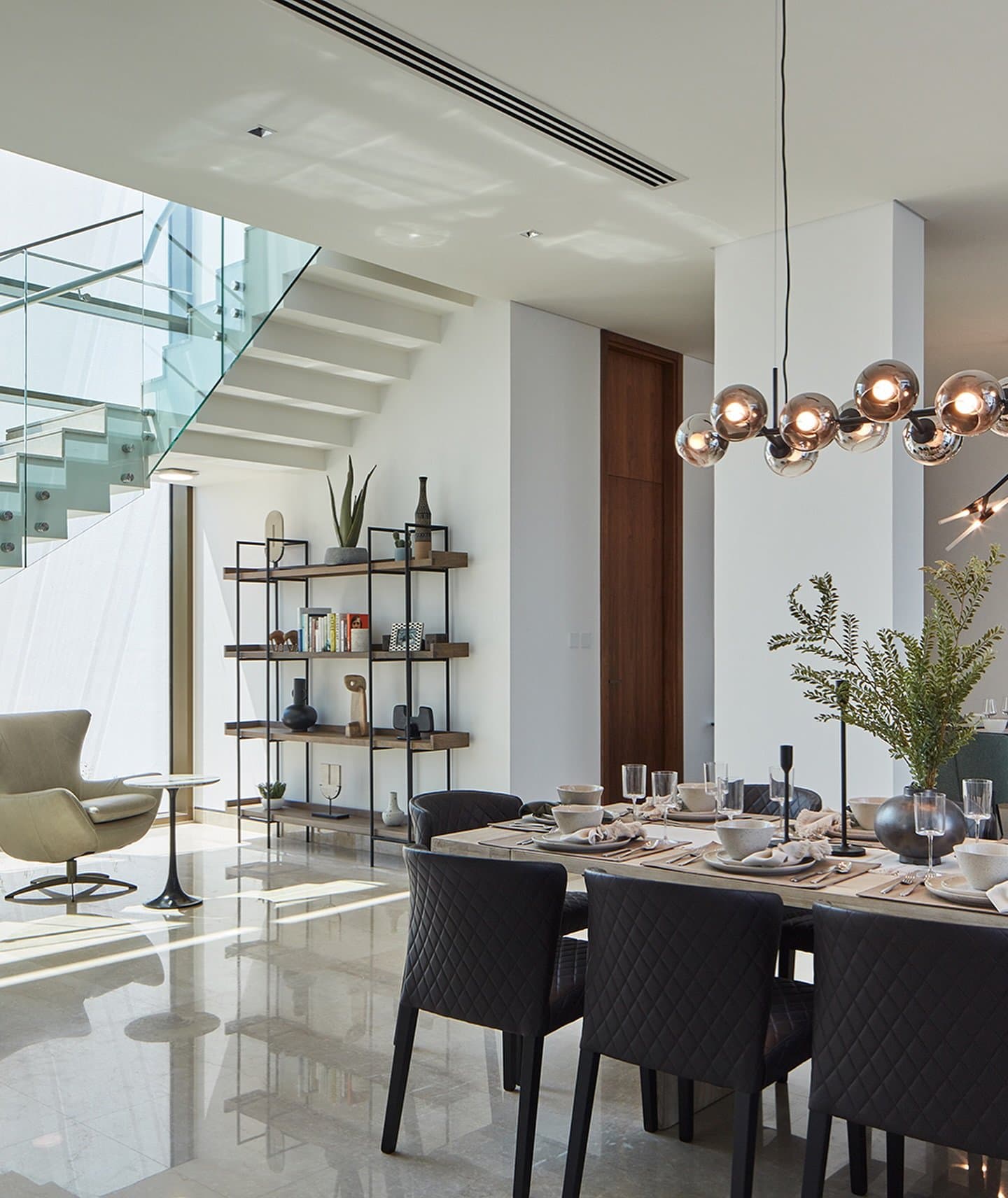 Spherical pendants and quilted leather chairs anchor the dining area beneath the floating staircase.