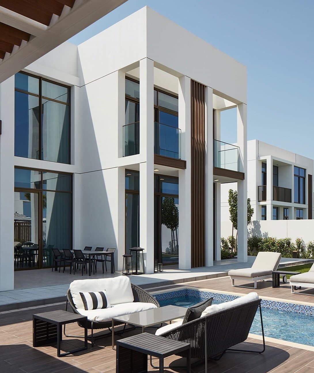 The villa's white volumes and vertical wood fin meet the terrace, plunge pool, and shaded pergola.