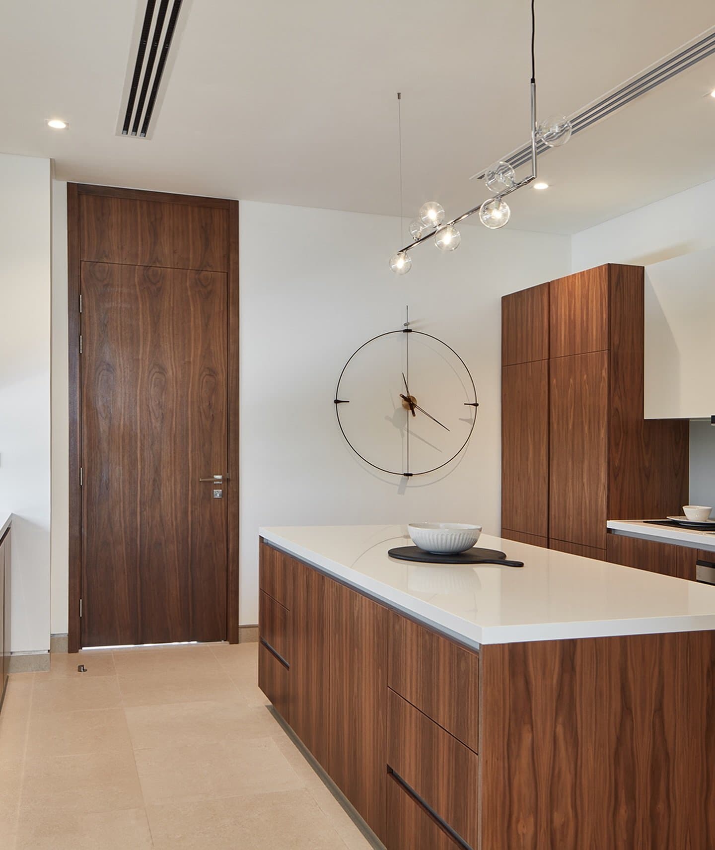 A walnut-veneer island and matching pantry door define the kitchen's pared-back palette.