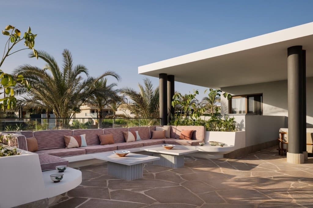 On the rooftop terrace, a dusty rose sectional and slender black columns balance softness against architectural geometry.