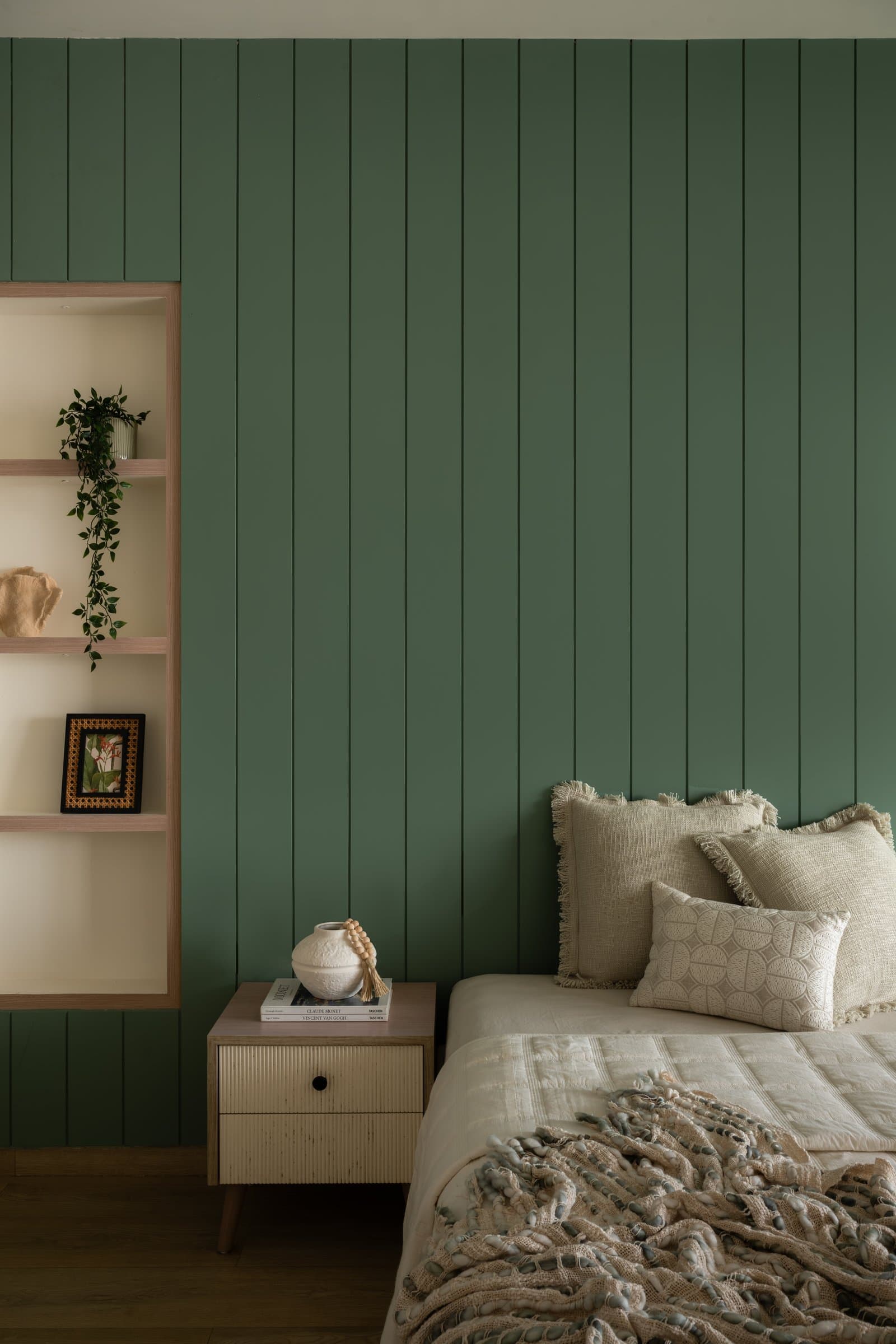 In the second bedroom, vertical green panelling establishes a distinct tonal direction from the pale interiors elsewhere
