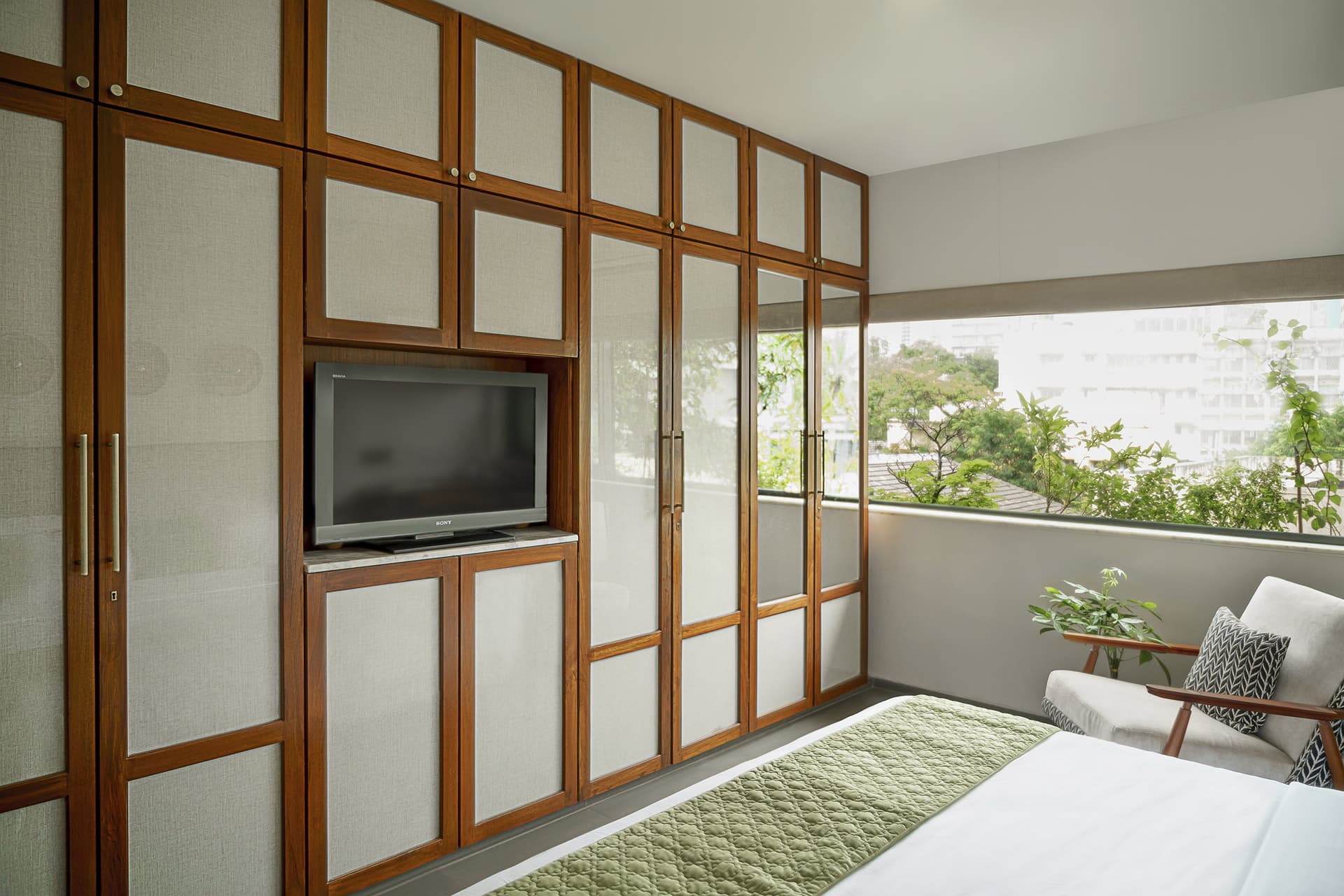 The second bedroom, where a full wall of wood-and-fabric joinery integrates wardrobe and media into one plane