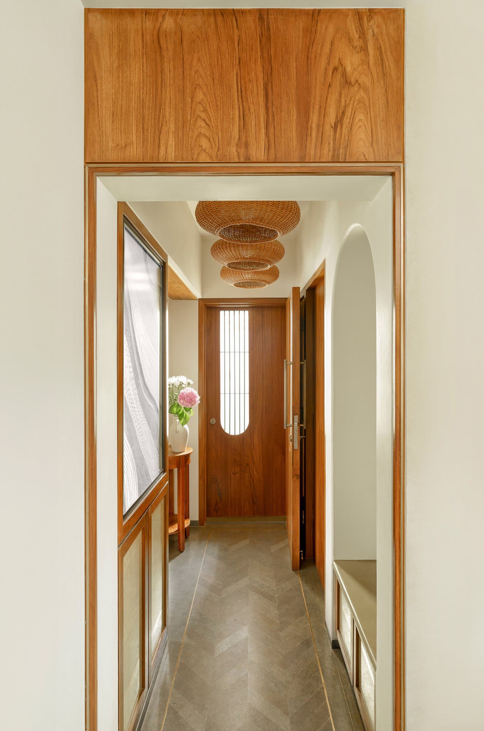The entry passage, framed by warm wood and a cluster of woven pendants, sets the material grammar of the home