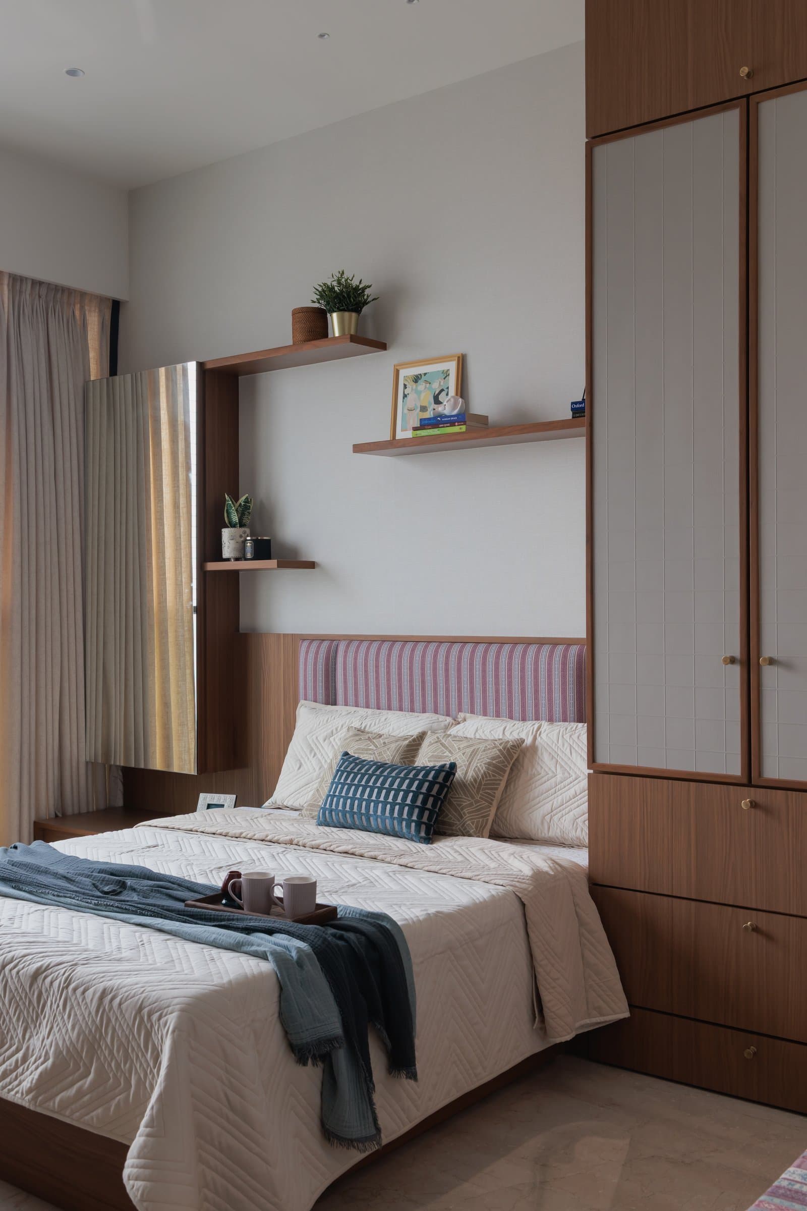 In one bedroom, a striped upholstered headboard sits between a floor mirror and a cane-inset wardrobe