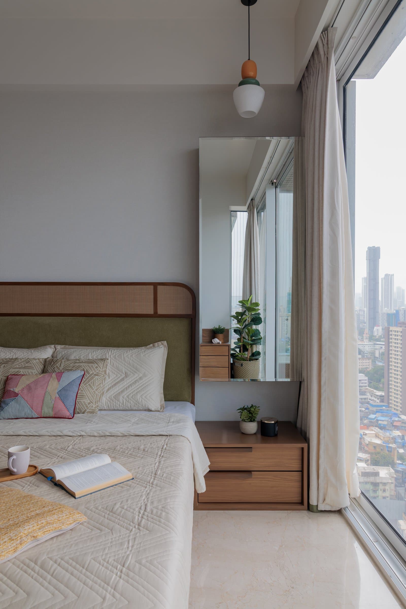 The parents' bedroom, quietly composed around a cane-and-upholstery headboard and a wide city view