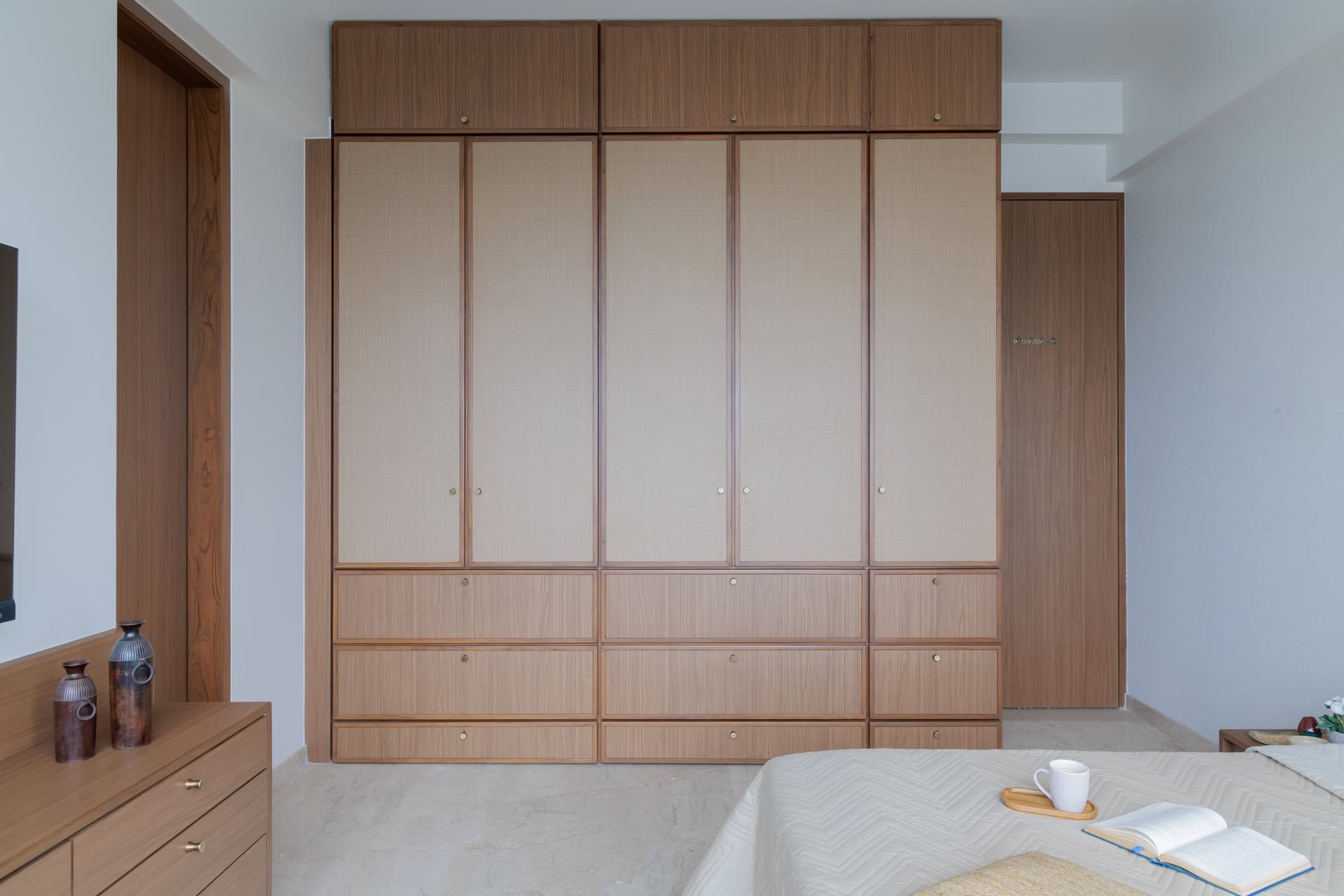 A full wall of caned wardrobes in the parents' room, softening the mass of storage with texture and warmth
