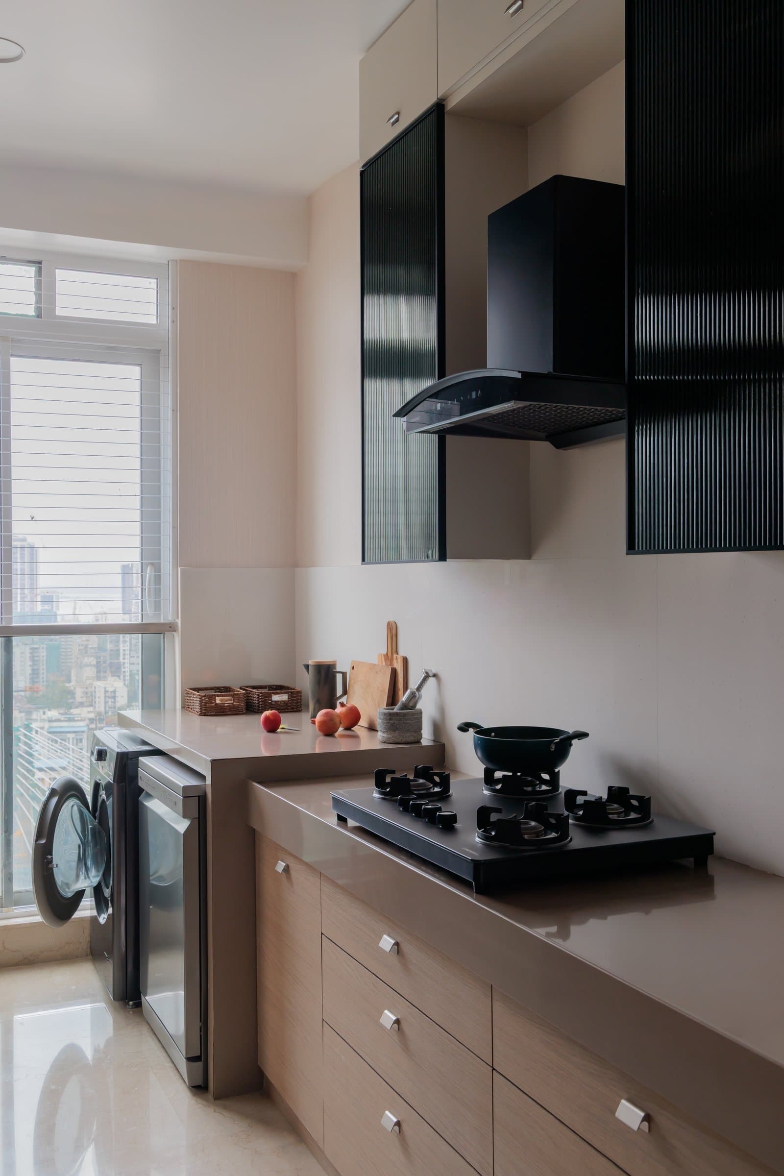 The kitchen adopts a utilitarian register, with pale timber cabinetry and reeded dark upper units echoing the dining buffet