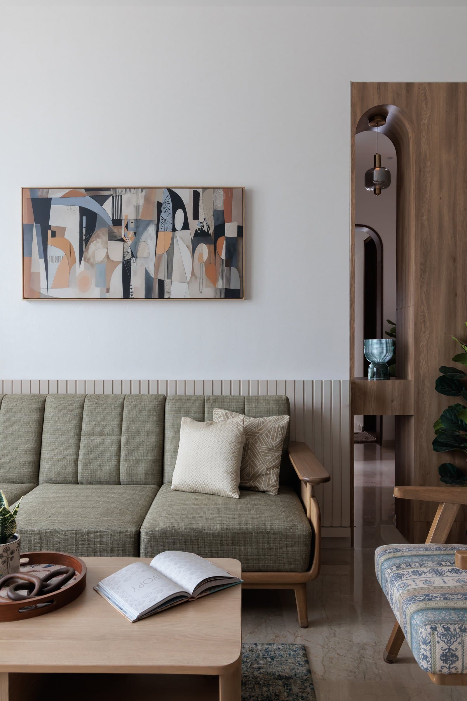 The framed abstract painting above the sofa sets the home's tonal register; beyond, an arched timber-lined opening extends the eye into the passage