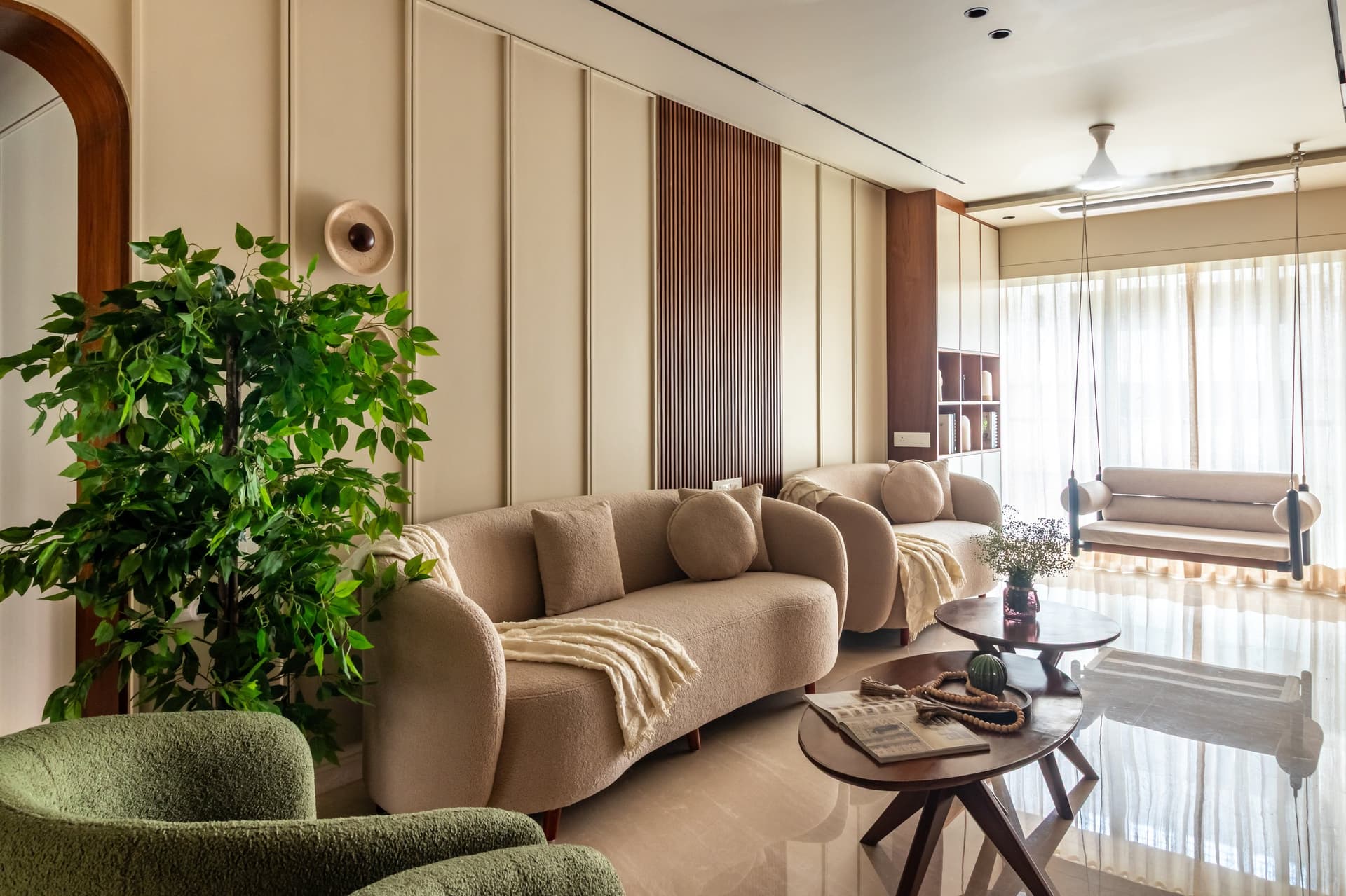 The living room, anchored by curved bouclé sofas and moss-green armchairs against a panelled ivory wall