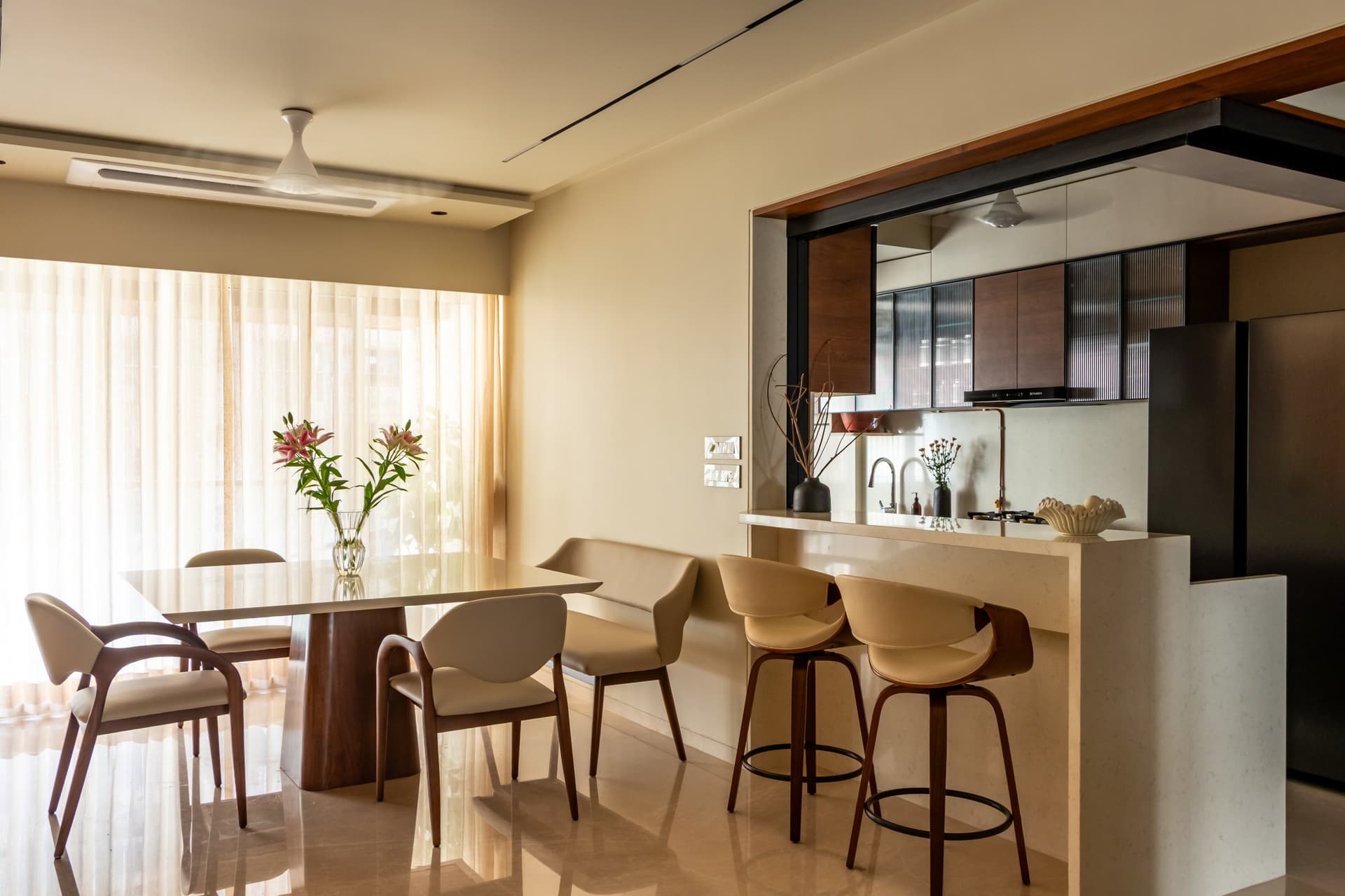 The dining area, its sculpted table and curved-back chairs set beside a stone-clad breakfast counter that extends from the open kitchen