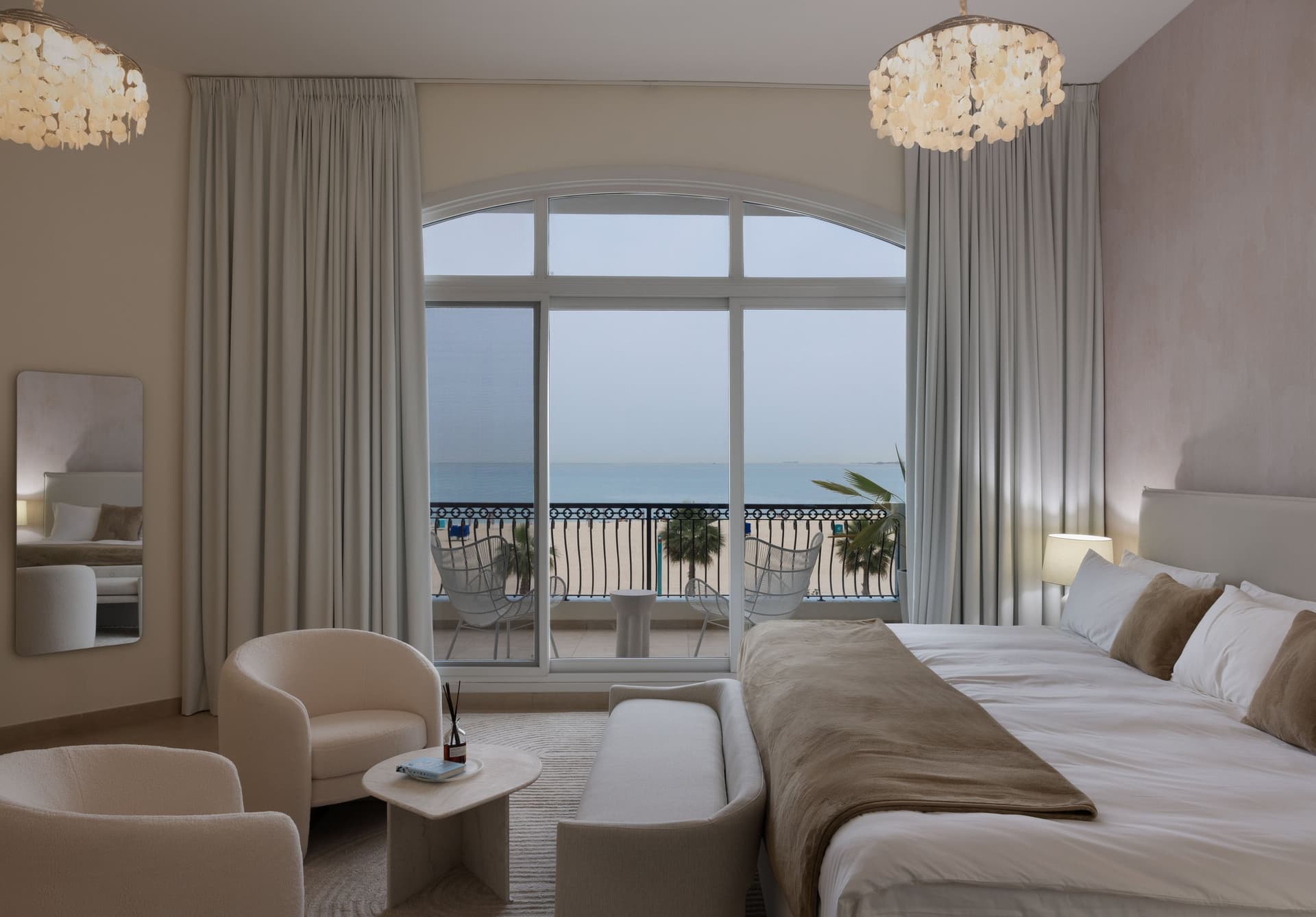 The main bedroom, oriented toward the sea through a tall arched window, with the custom three-metre bed sitting inside a hushed palette of sand and ivory