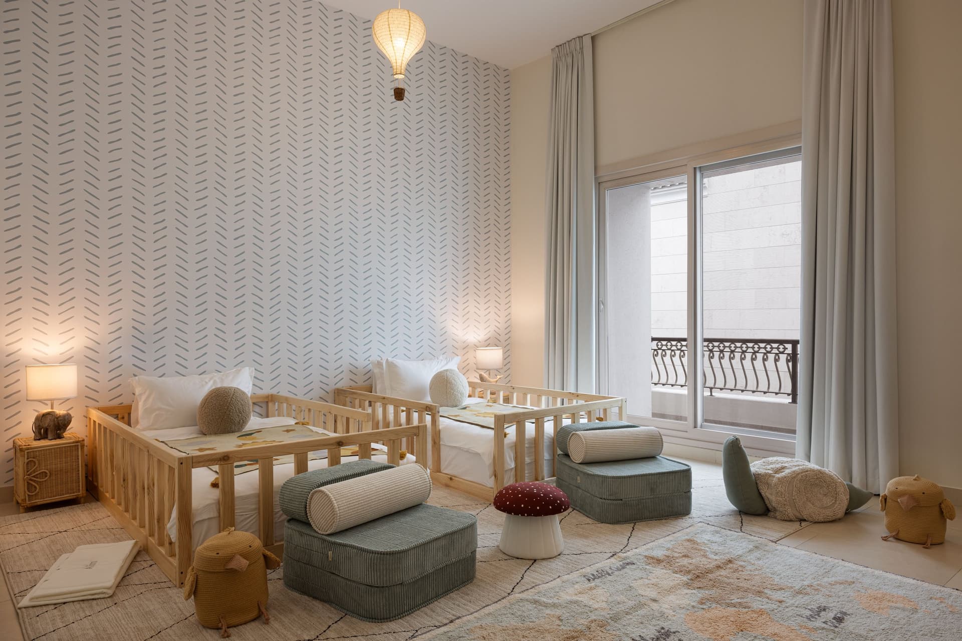 The children's shared room, anchored by two pine daybeds against a wall of hand-drawn dash pattern in soft blue, a woven hot air balloon pendant floating above