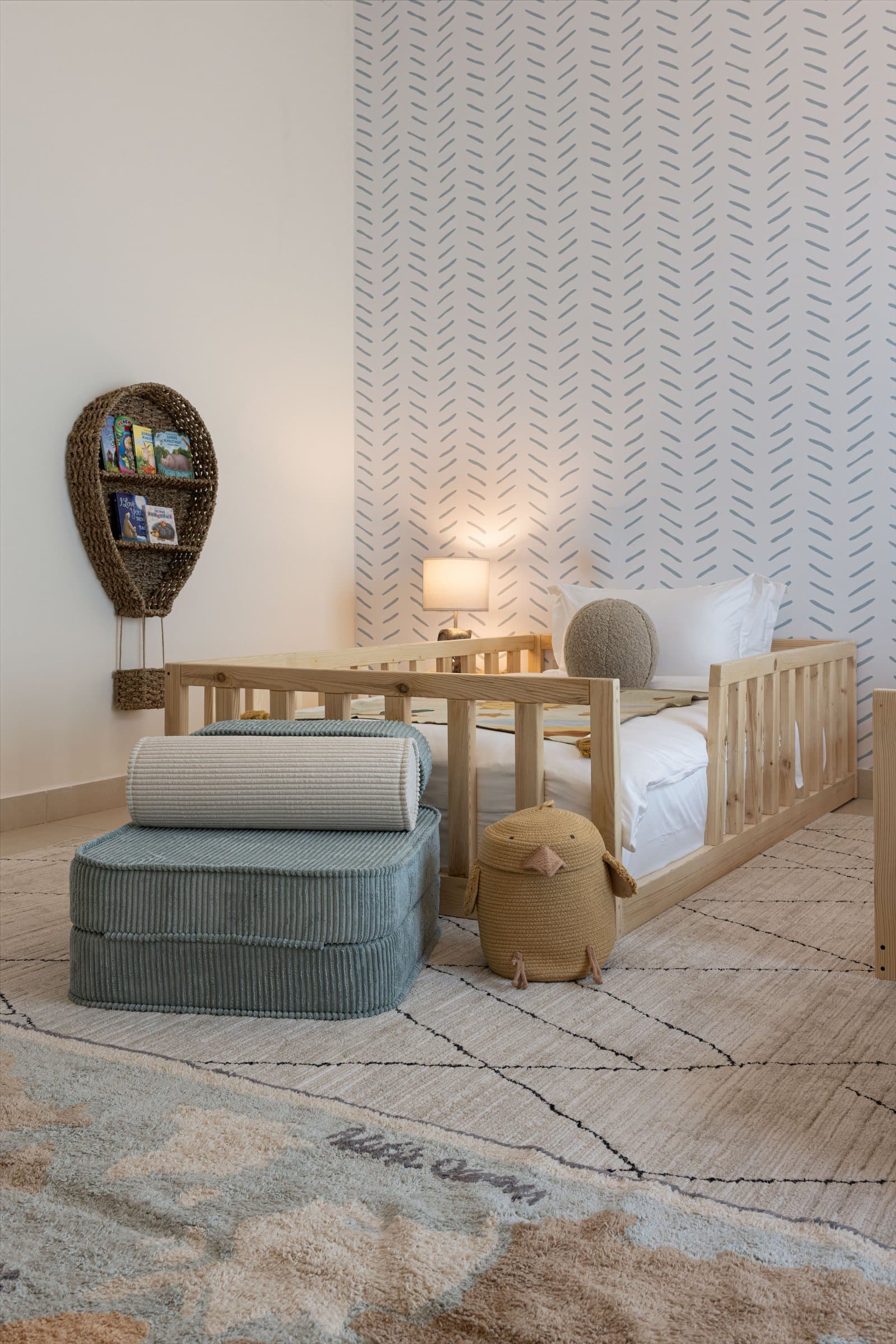A closer view of the pine daybed, corduroy pouf, and rattan wall pocket in the form of a hot air balloon holding picture books