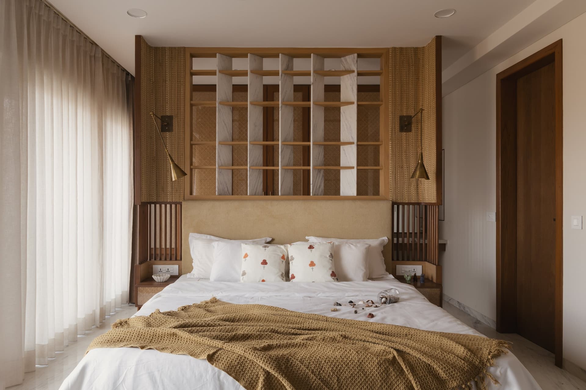 The second bedroom's headboard wall, composed of marble-and-oak gridded shelving, cane panels and articulated brass sconces