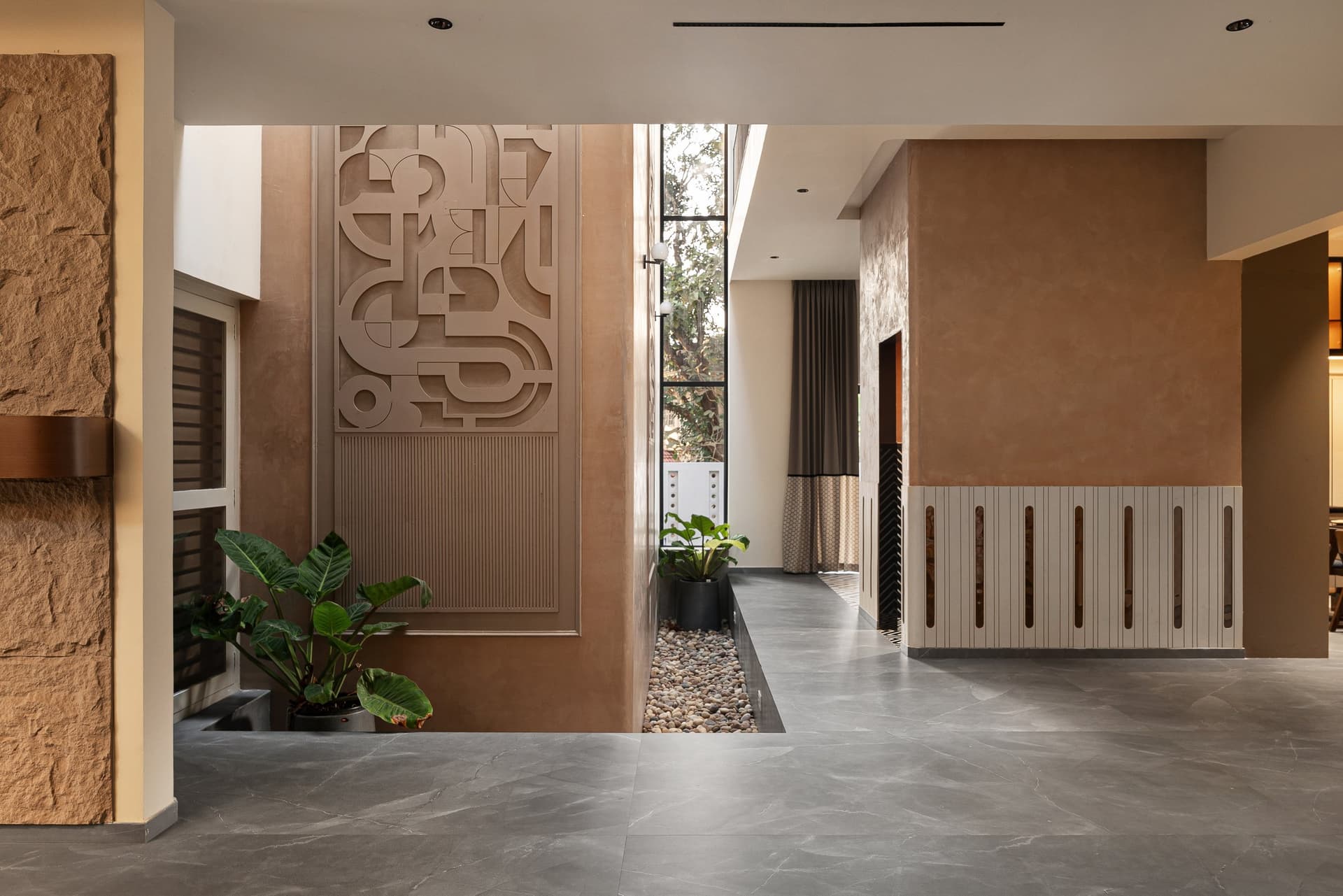 The entry foyer, where a sculpted relief panel rises beside a vertical slot of glazing that draws light into the heart of the plan