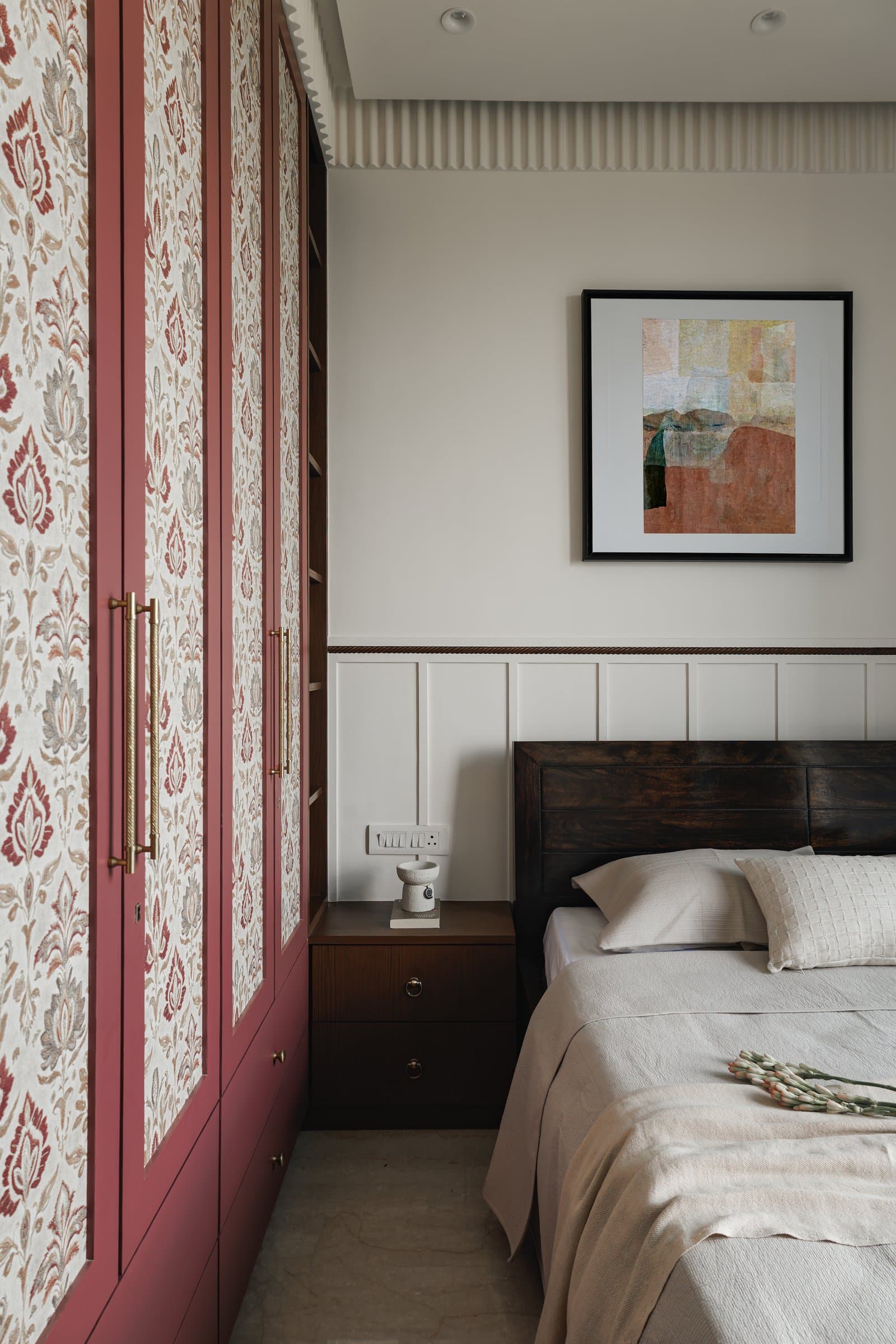 The second bedroom, where a deep rose wardrobe inlaid with patterned panels sits against white wainscoting