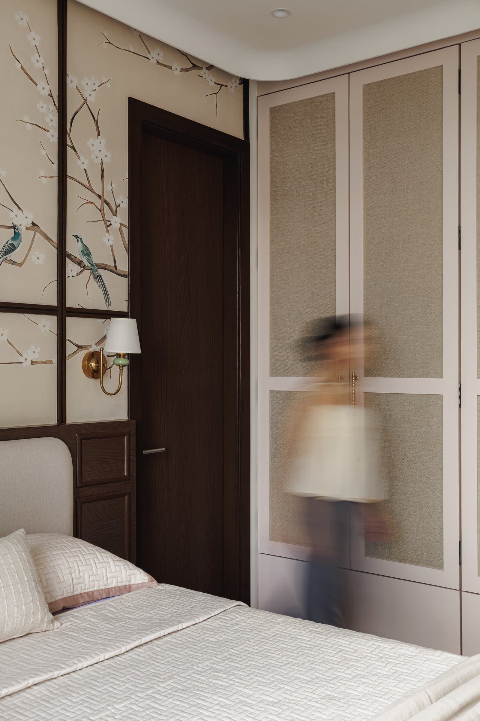 A view across the primary bedroom, where linen-finish wardrobe panels in dusty blush meet the darker panelled wall