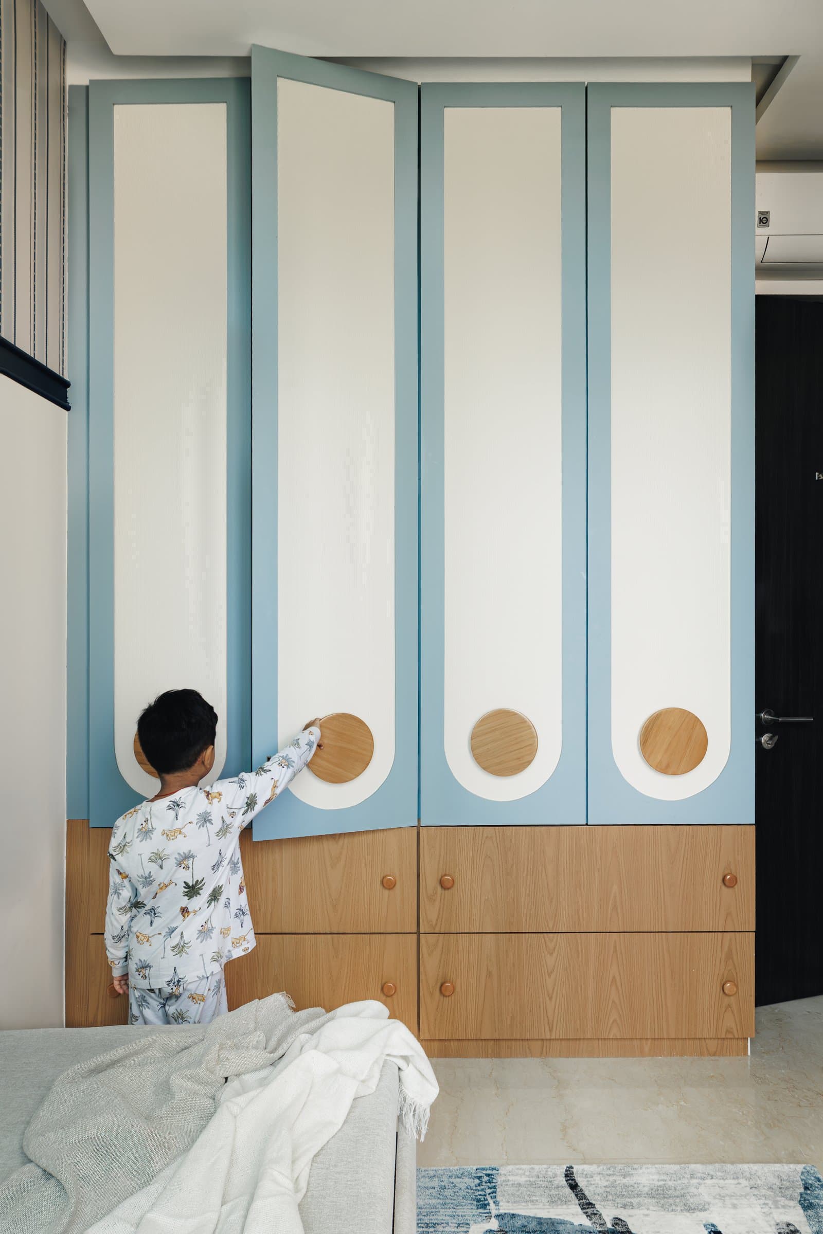 The wardrobe wall, its ivory shutters framed in powder blue with circular wood pulls