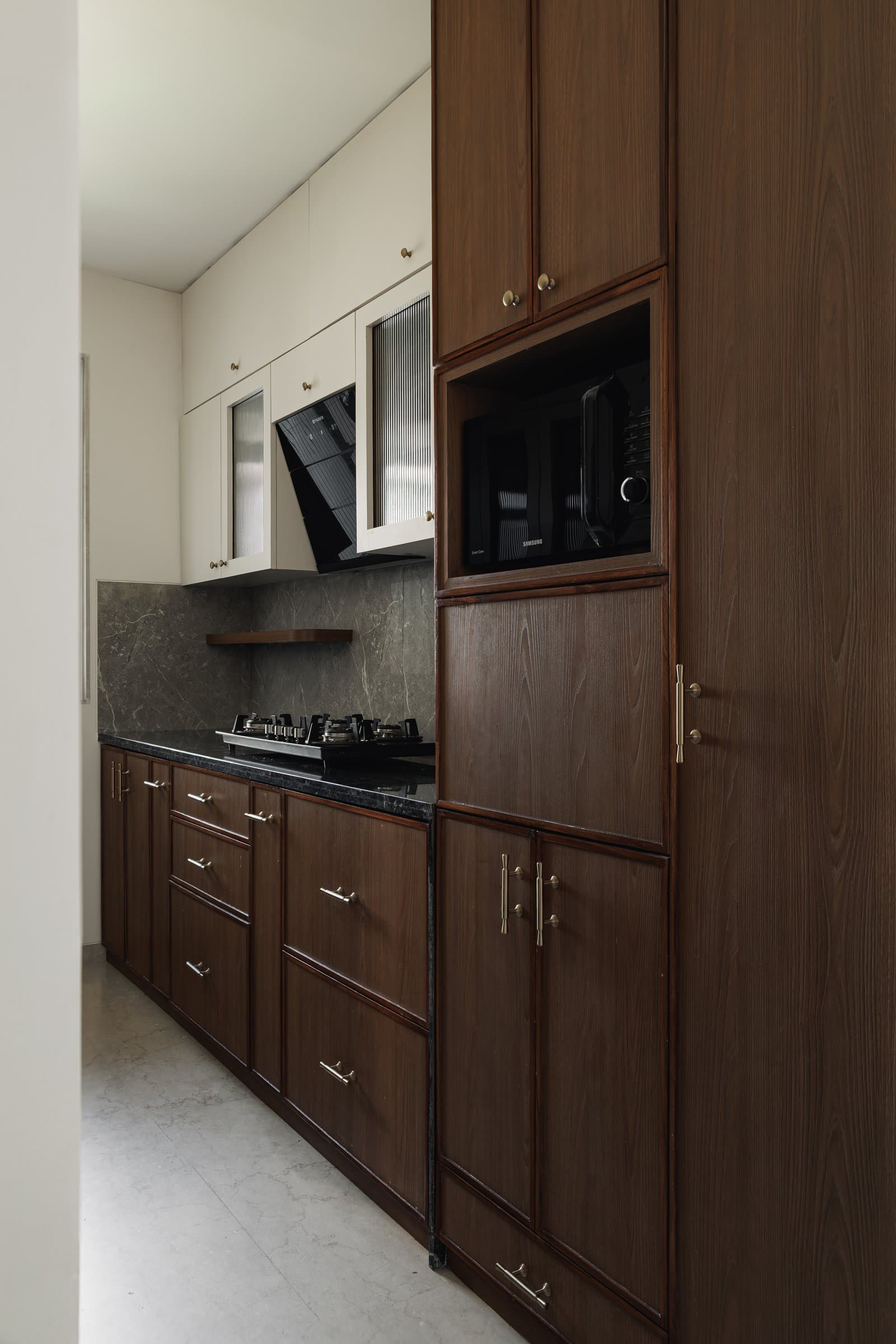 The galley kitchen, where dark wood-toned cabinetry meets ivory uppers with reeded glass fronts
