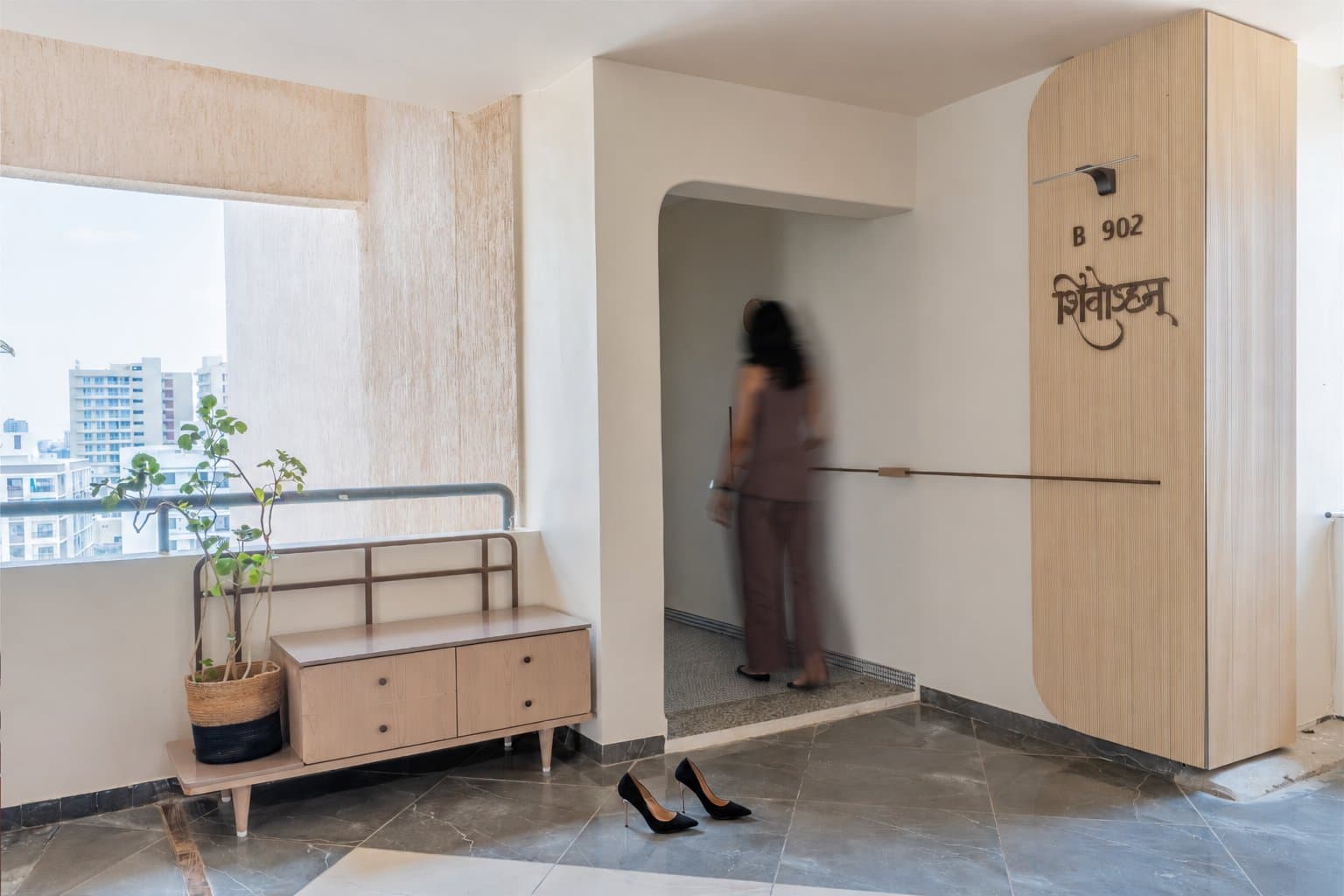 The arrival threshold, where a reeded panel carries the home's name in Devanagari and a mosaic inset marks the shift from corridor to private realm
