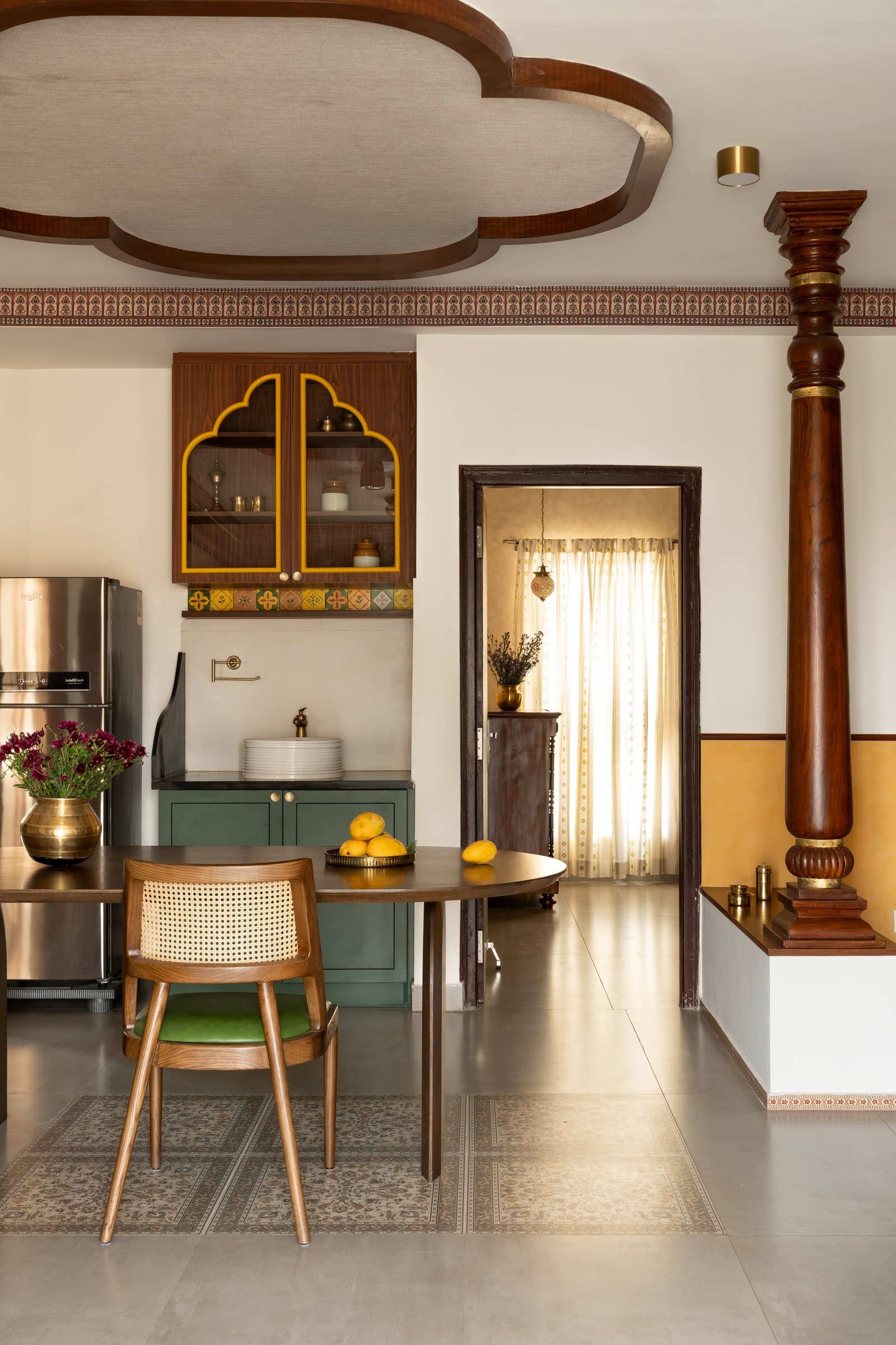 The dining area, where an oval wooden table on sculpted arched bases sits beneath the scalloped ceiling detail