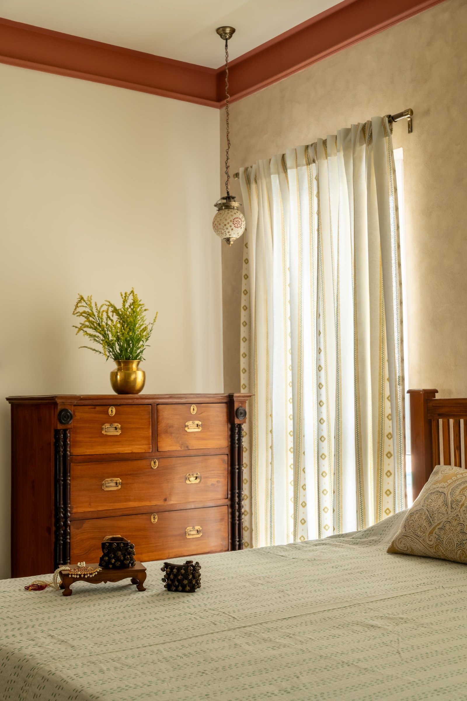 In the master bedroom, a vintage wooden chest with brass campaign-style hardware sits beneath a Moroccan-style pendant