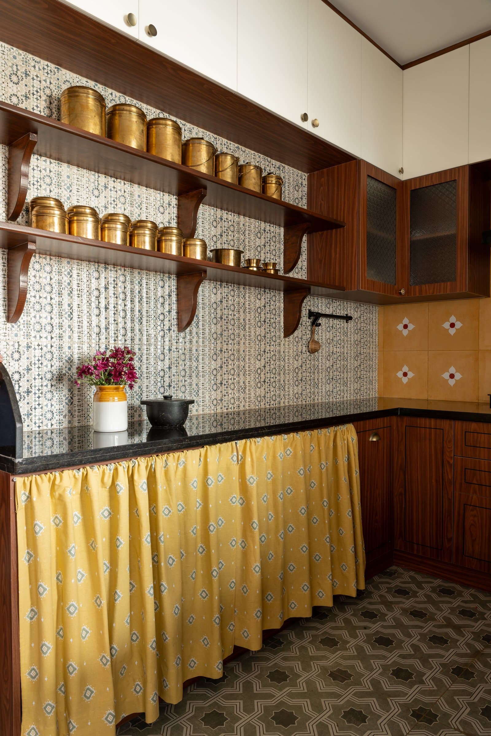Open shelving along one wall holds a collection of brass utensils against the patterned tiled backdrop