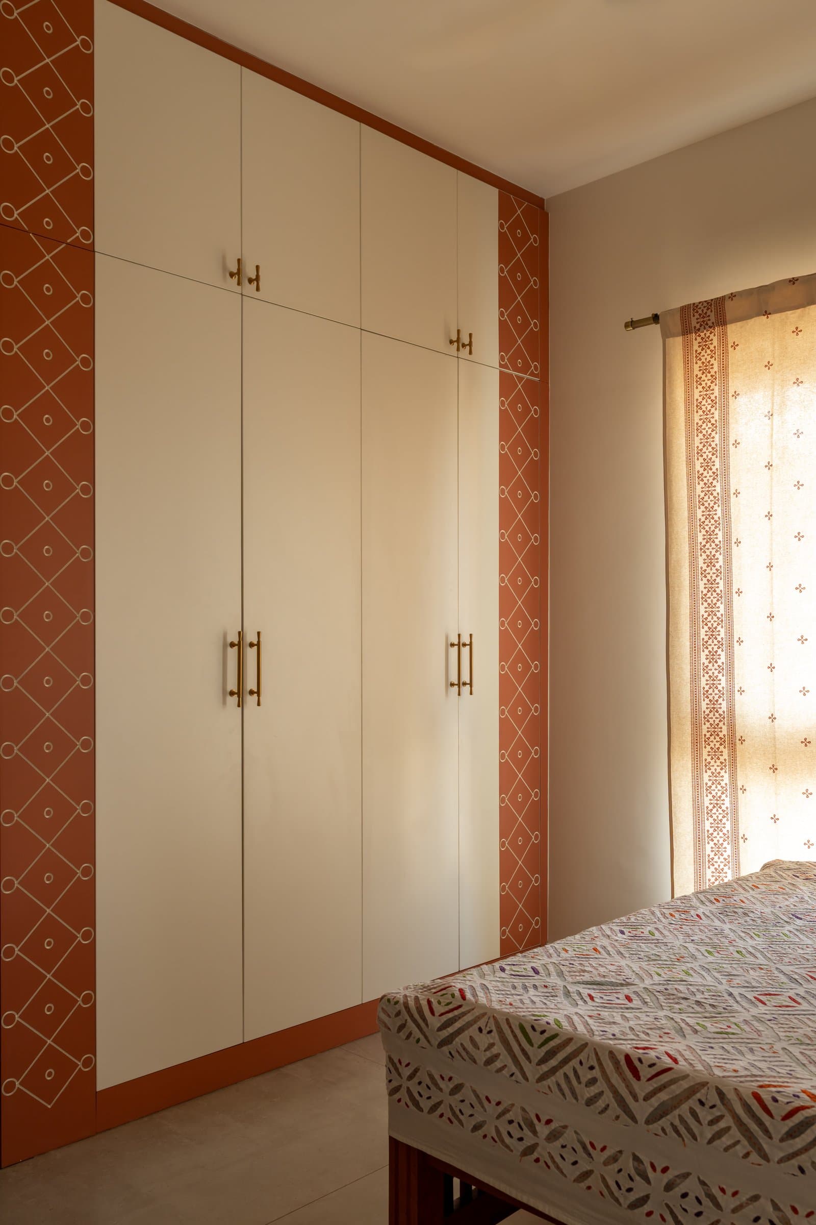 The guest bedroom wardrobe, where ivory shutters framed in terracotta carry a kolam-inspired motif in fine white linework