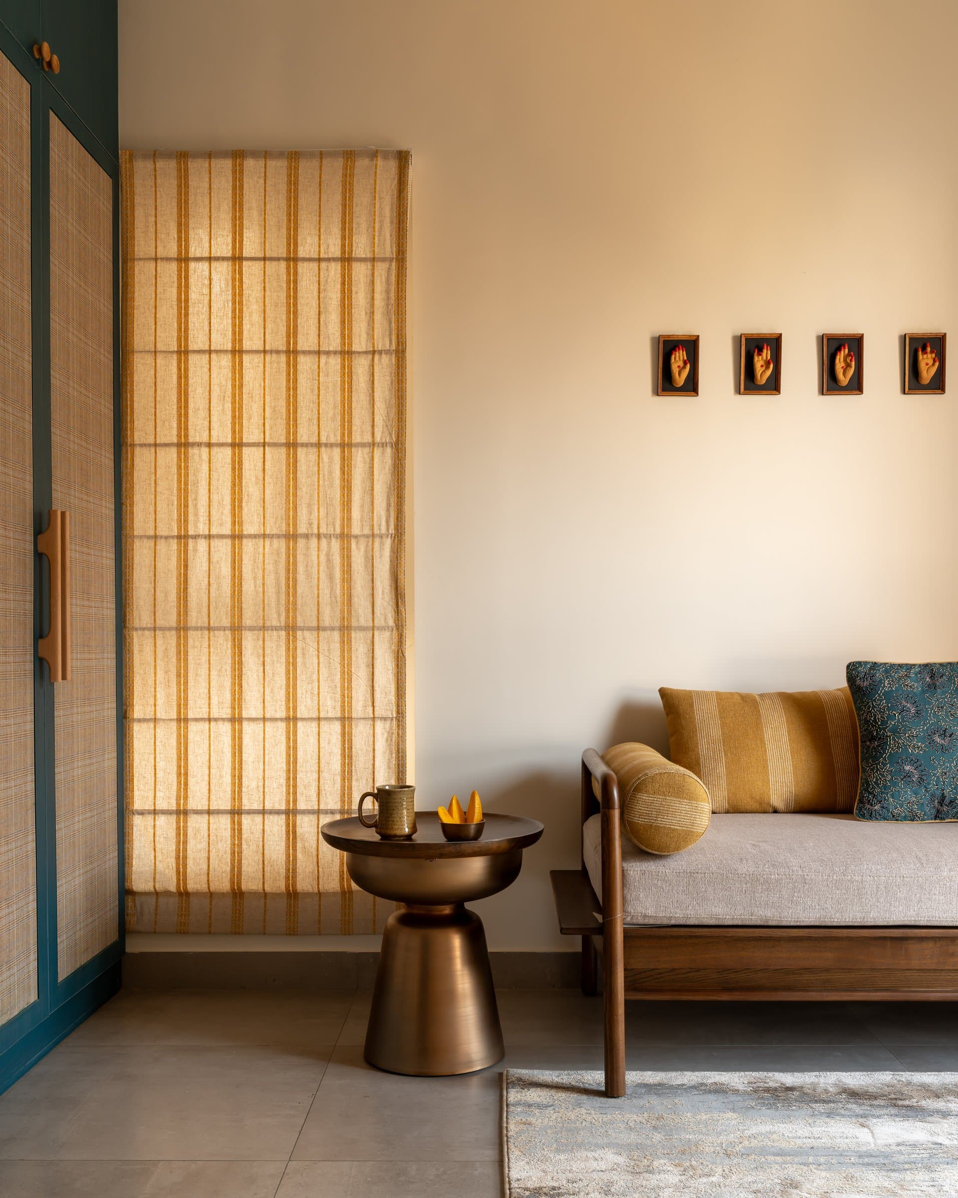 A wooden daybed with linen cushions and striped bolsters, beneath four small framed reliefs of Bharatanatyam hand gestures