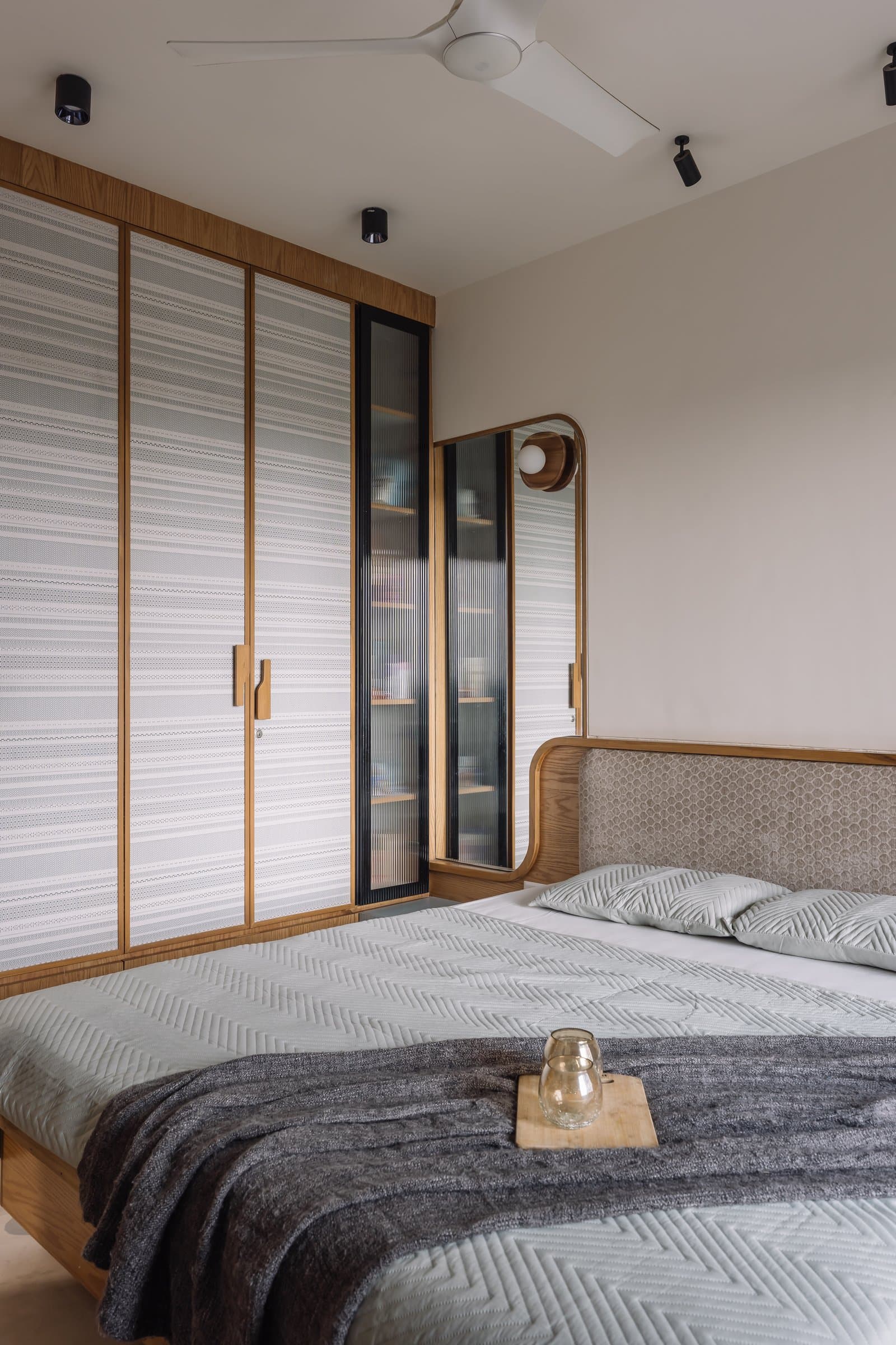 A wider view of the wardrobe wall in the primary bedroom, balanced through warm wood framing and slim reeded-glass panels