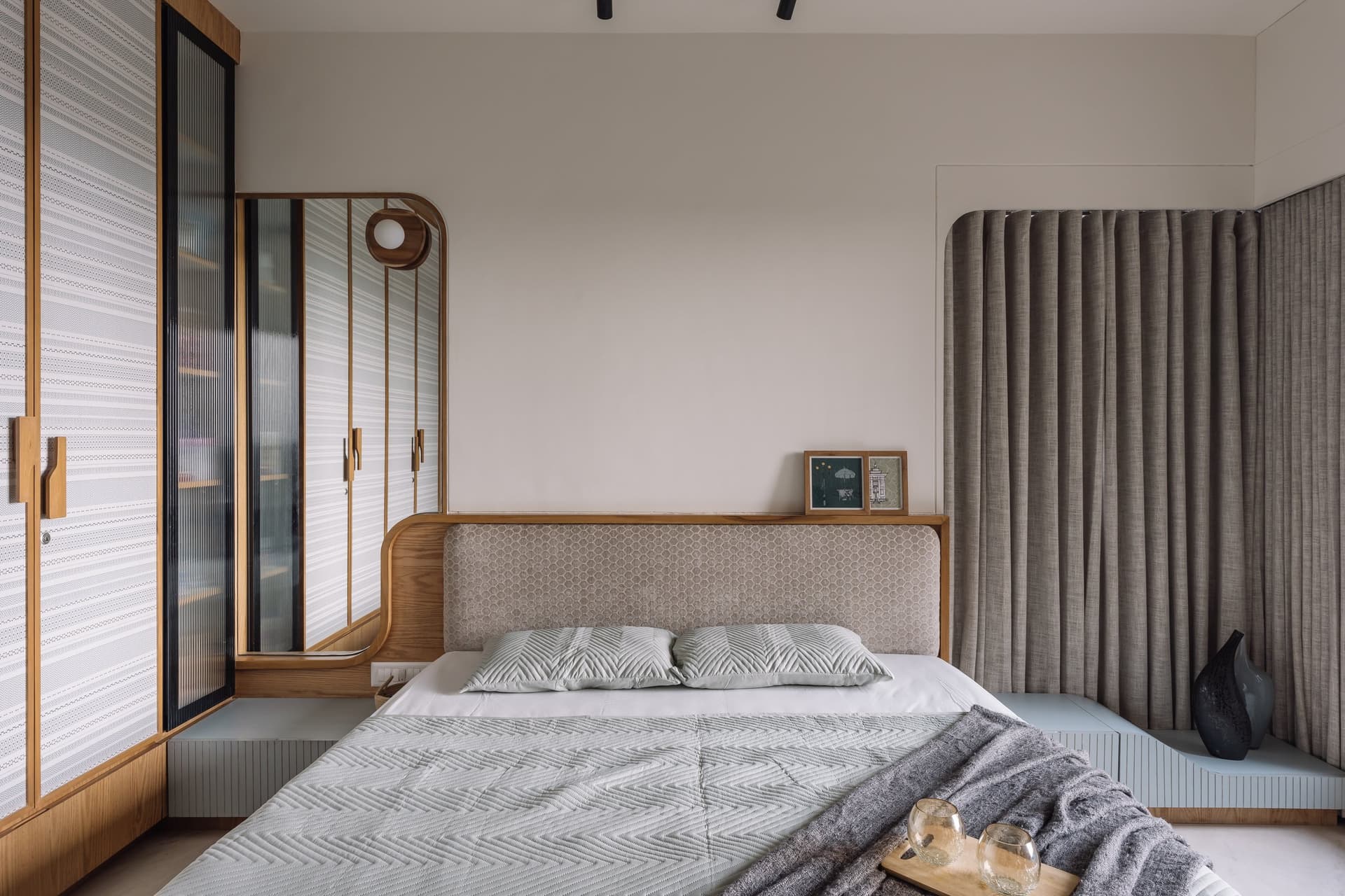 The primary bedroom, where an upholstered honeycomb-textured headboard is held within a curved wooden frame that extends into integrated bedside ledges