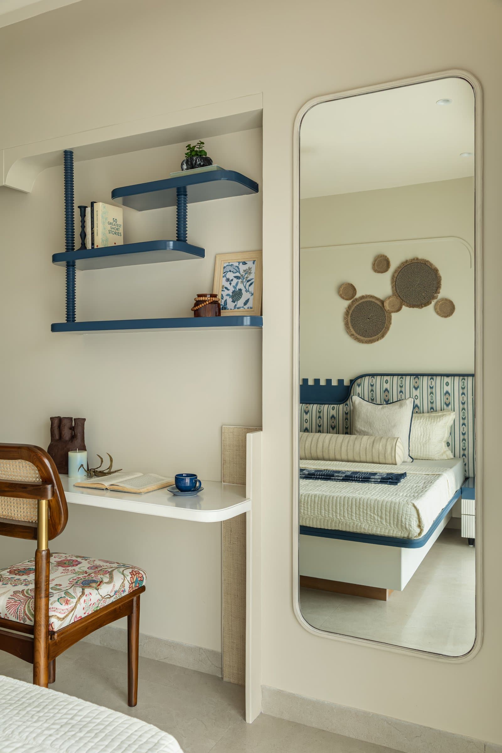 A compact study nook within the second bedroom, with a wall-mounted desk and cane-backed chair beneath indigo shelves