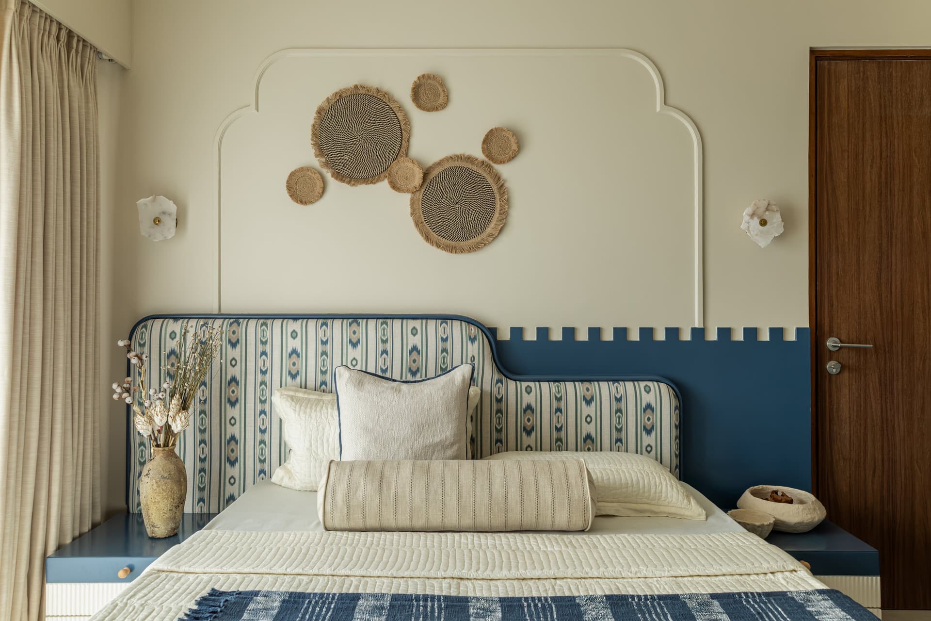The second bedroom, where a scalloped wall contour and an indigo-and-ivory headboard introduce a cooler, more graphic register