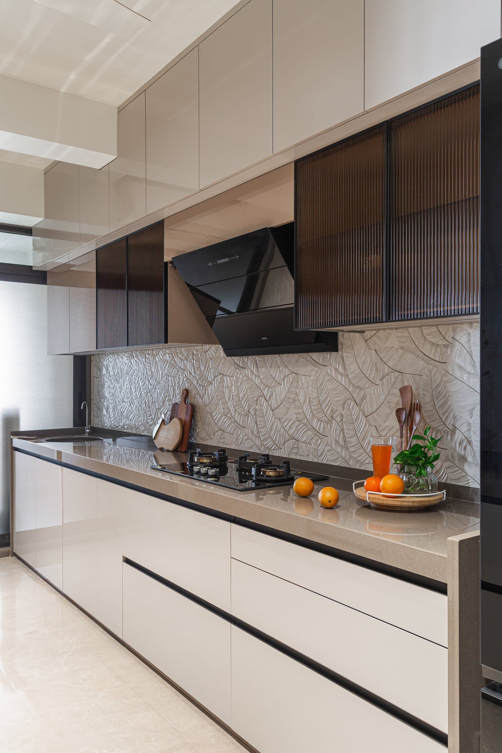 The kitchen, where glossy cream cabinetry meets reeded dark glass uppers and a textured leaf-motif backsplash